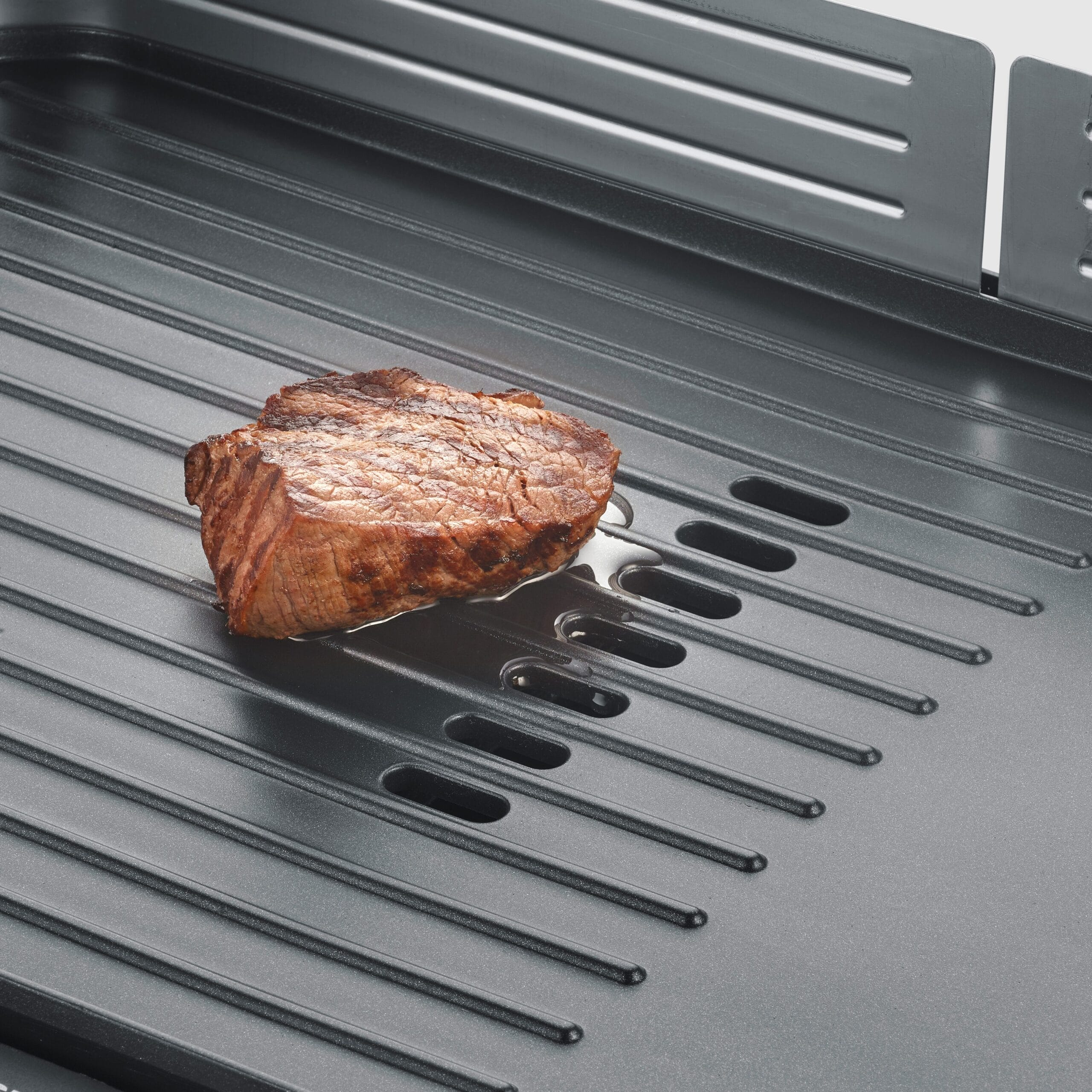 A seared steak rests on a grooved grill plate with rendered fat.