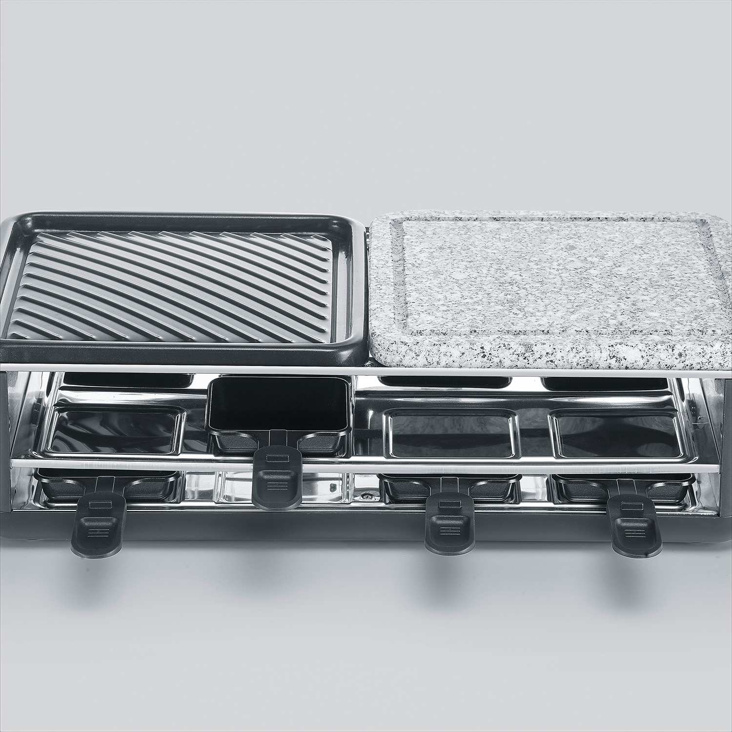 Een raclette grill met geribbelde grillplaat, steenplaat en pannetjes.