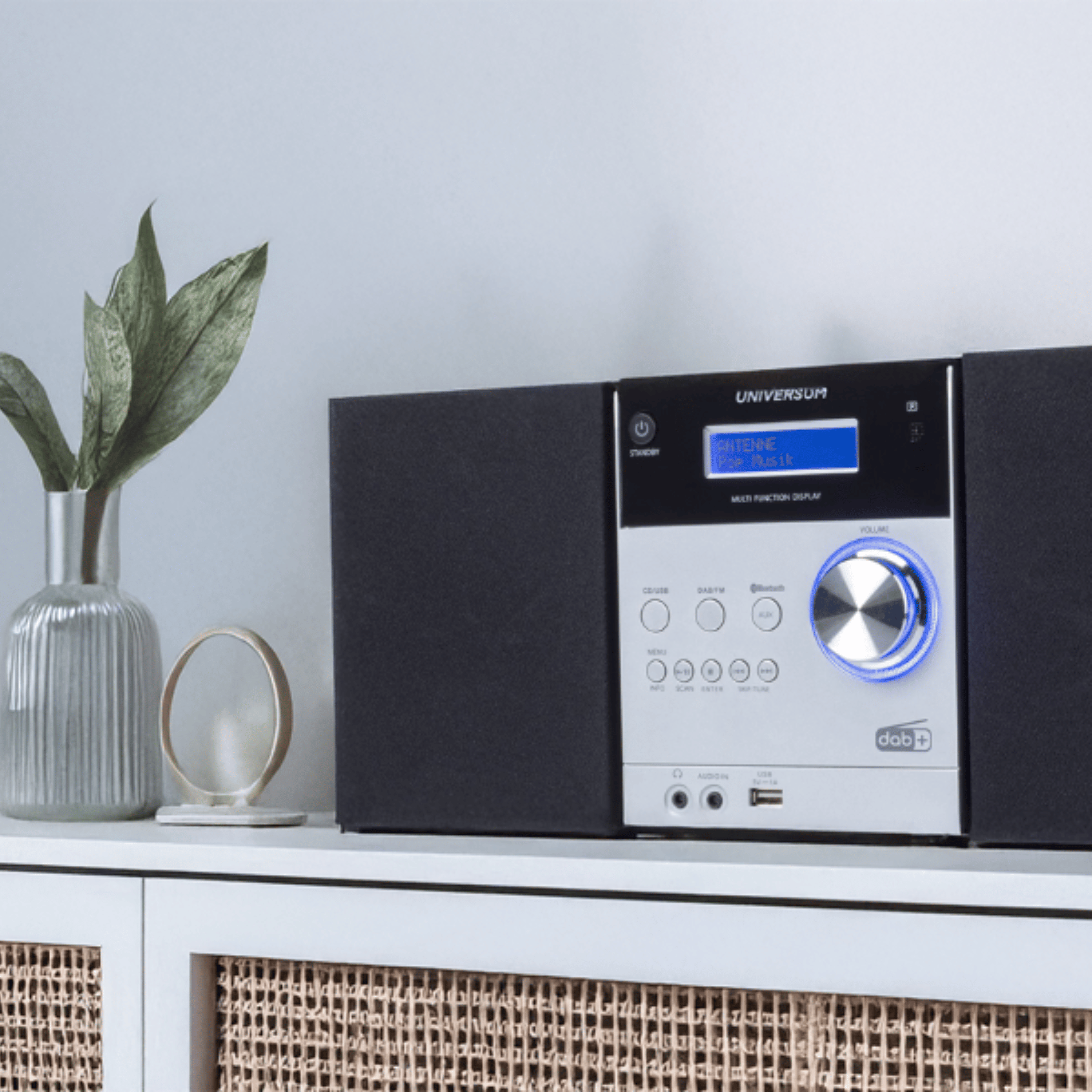 Ein modernes DAB+ Radio mit silbernem Drehregler und blauem Licht steht auf einem weißen Schrank.