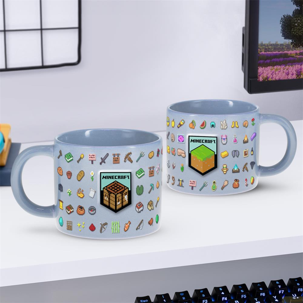 Zwei graue Minecraft-Tassen mit Pixelkunst-Symbolen und einem Werkbank auf einem weißen Schreibtisch.