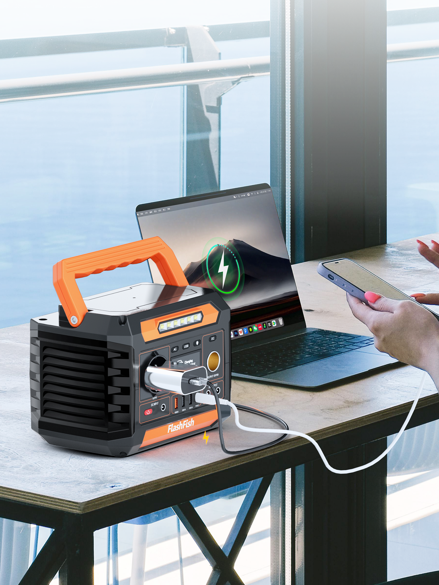 Una central eléctrica portátil con asa naranja, cargando un teléfono y un portátil.