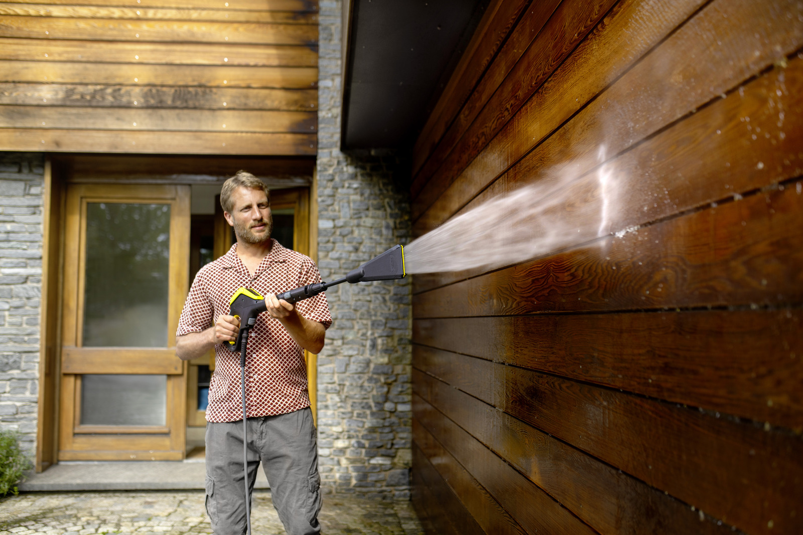 Man reinigt houten gevel met hogedrukreiniger. Water spuit op de muur.