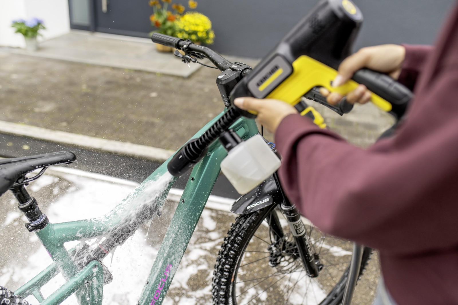 Eine Person sprüht ein türkisfarbenes Fahrrad mit einem gelb-schwarzen Hochdruckreiniger im Freien.