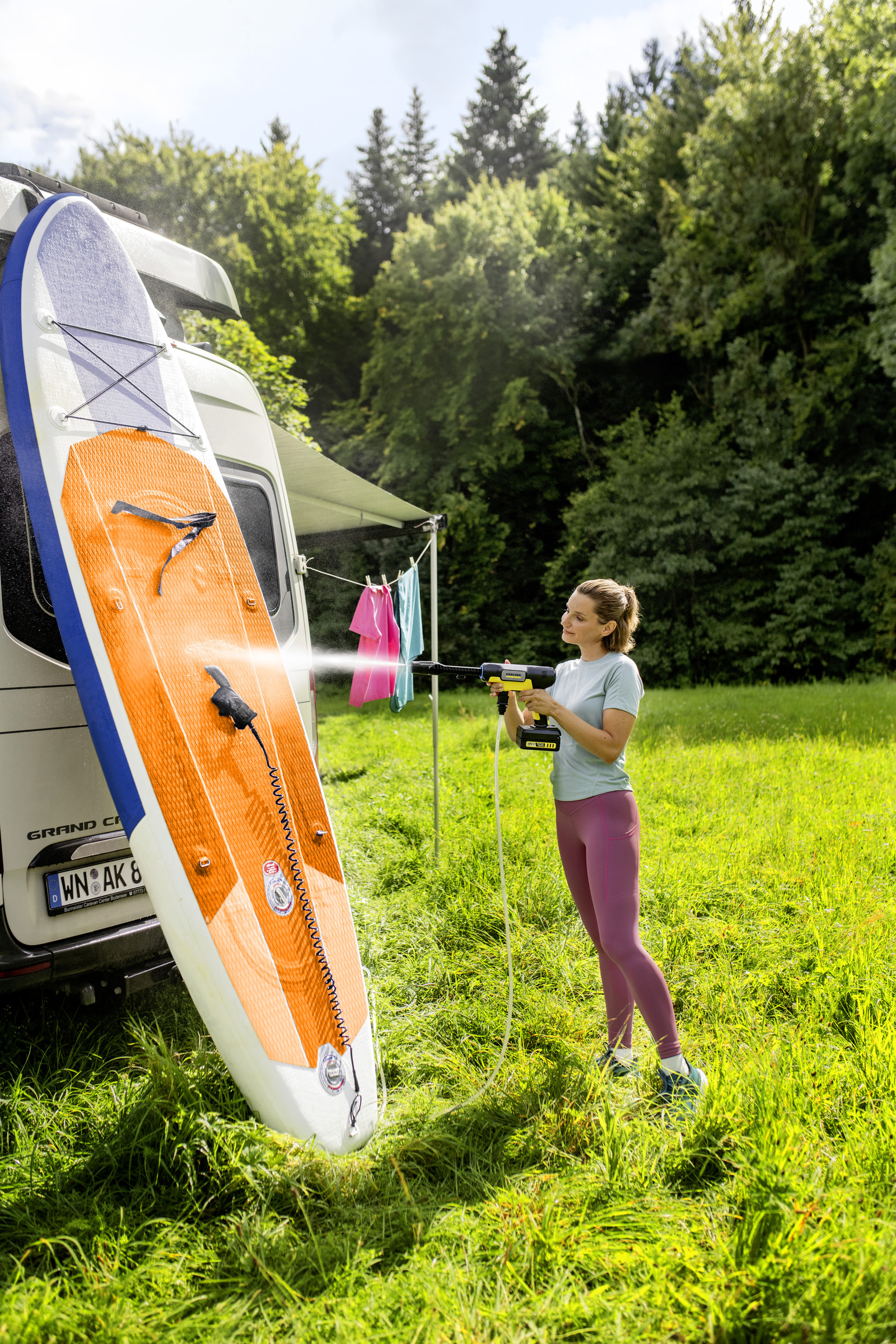 Eine Frau reinigt ein Stand-Up-Paddleboard mit einem Hochdruckreiniger neben einem Wohnmobil.