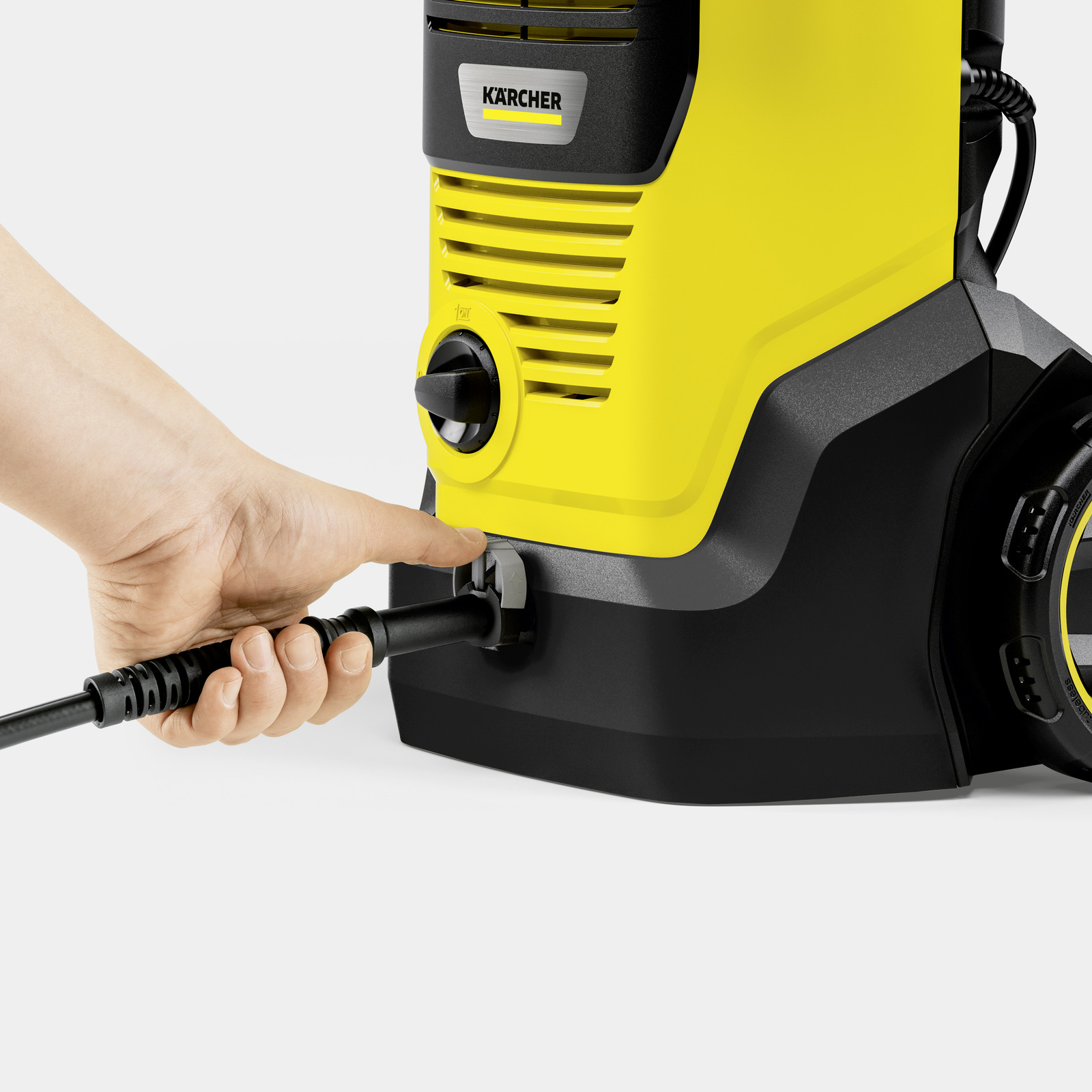 A hand inserts a black hose into a yellow pressure washer.