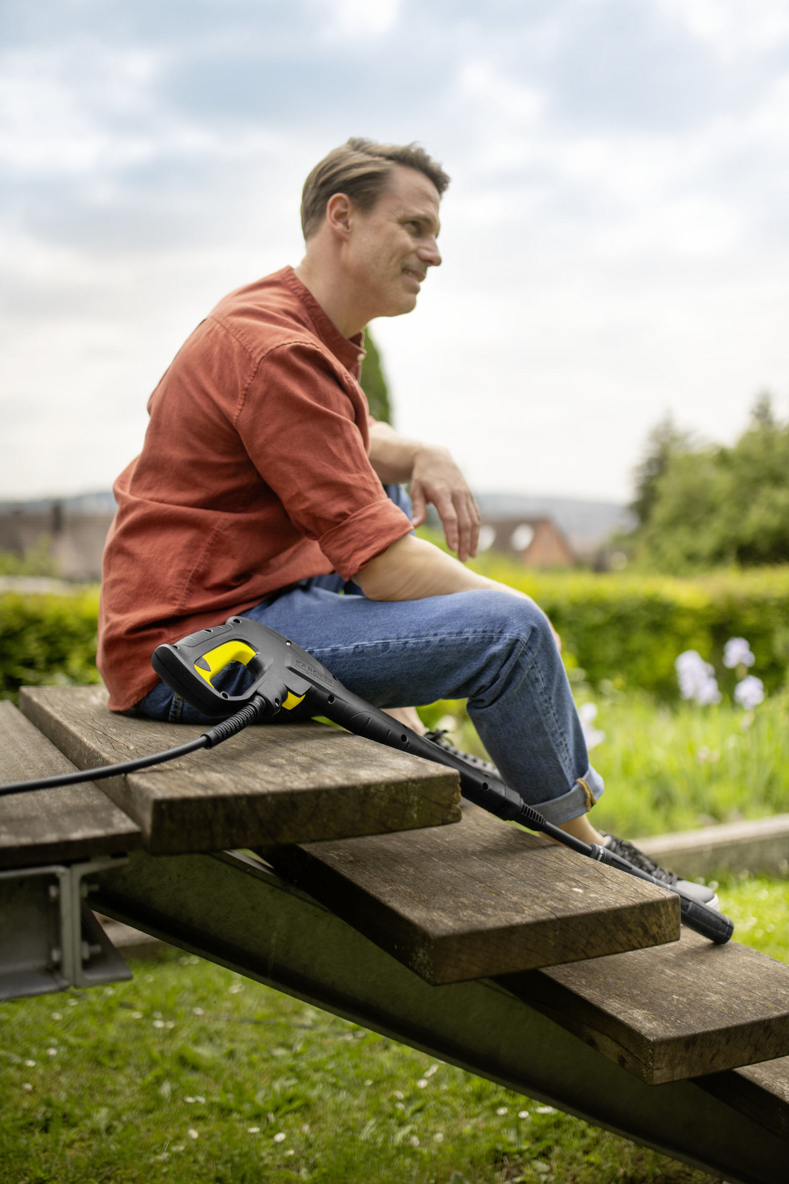 A man sits on a wooden bench with a pressure washer handle.
