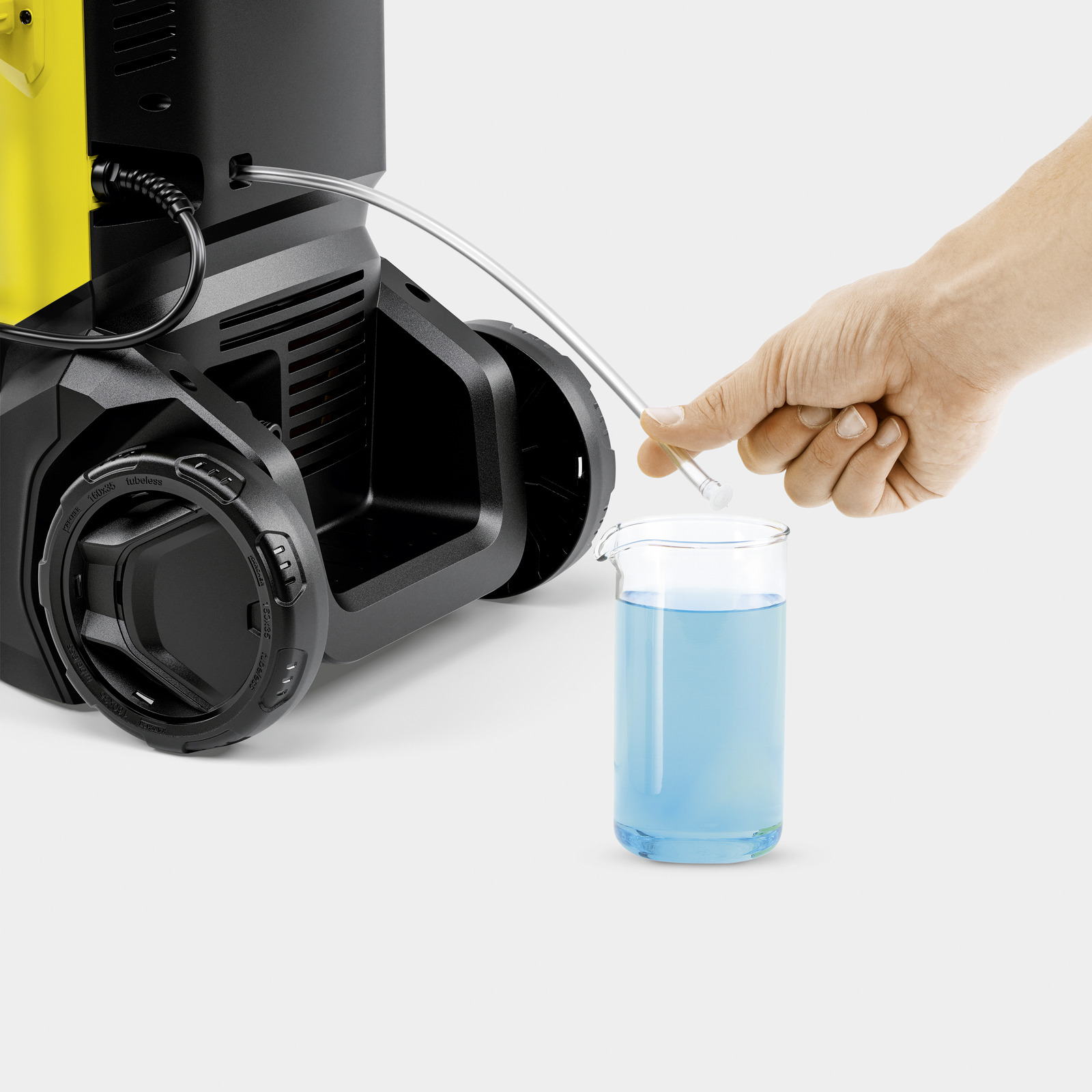 Eine Hand steckt einen klaren Schlauch in einen Becher mit blauer Flüssigkeit neben einer gelb-schwarzen Maschine.