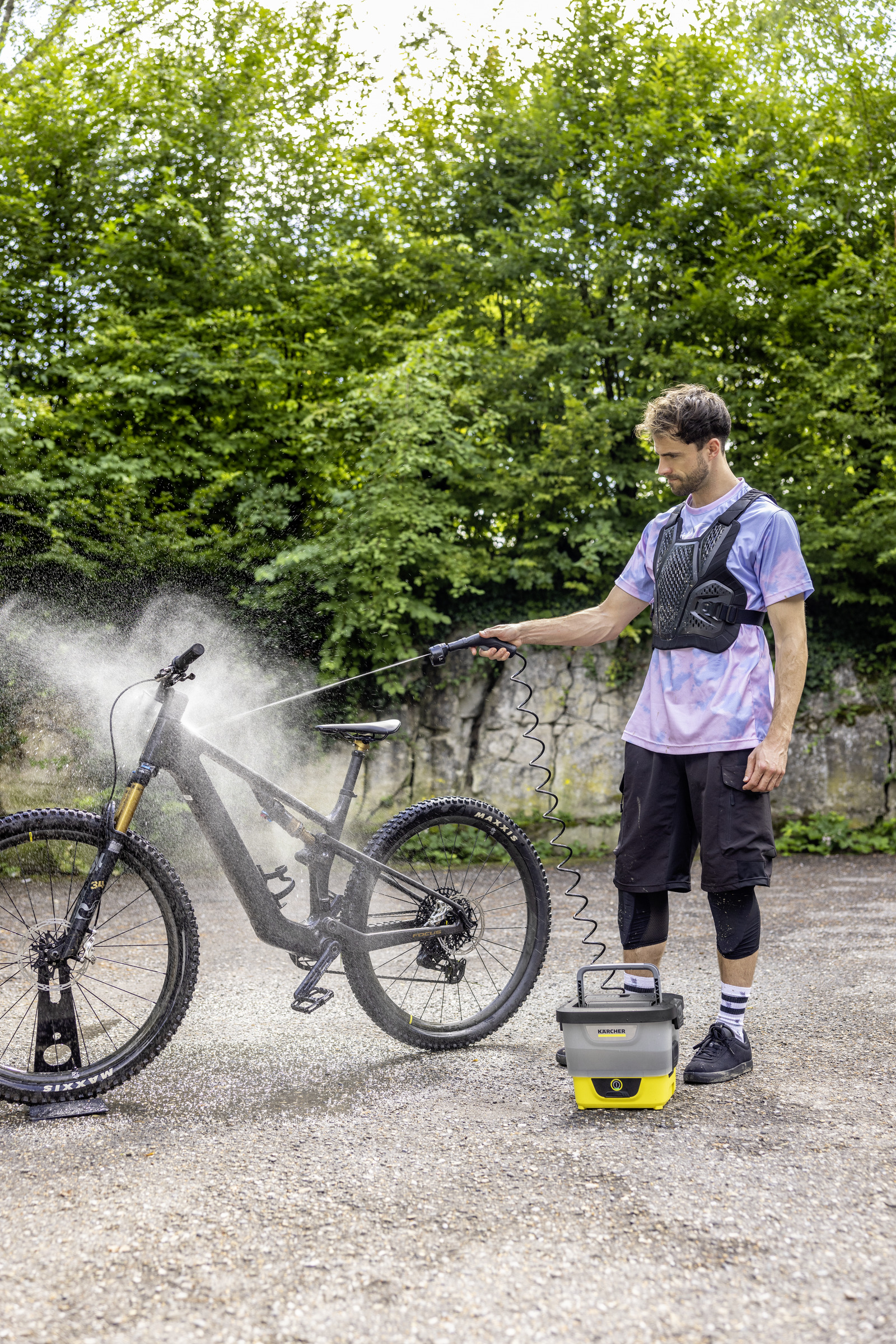 A man washes a mountain bike with a pressure washer outdoors.