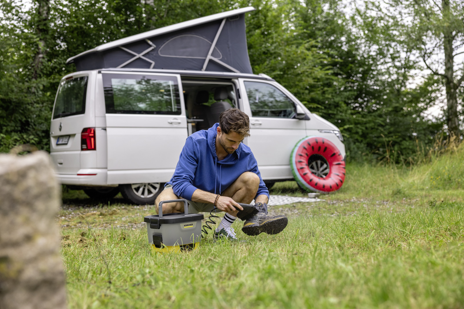 Man cleans shoe next to campervan with inflatable watermelon.