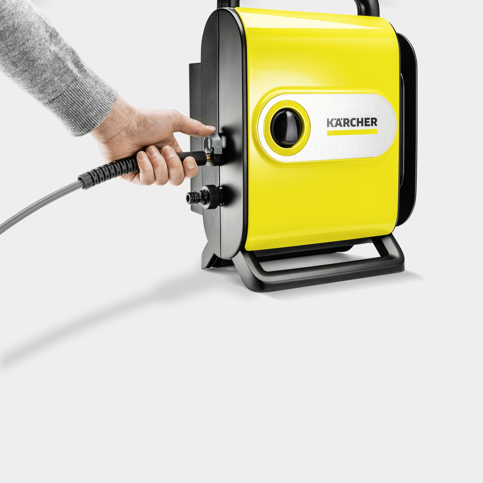Een hand sluit een slang aan op een gele Kärcher machine.