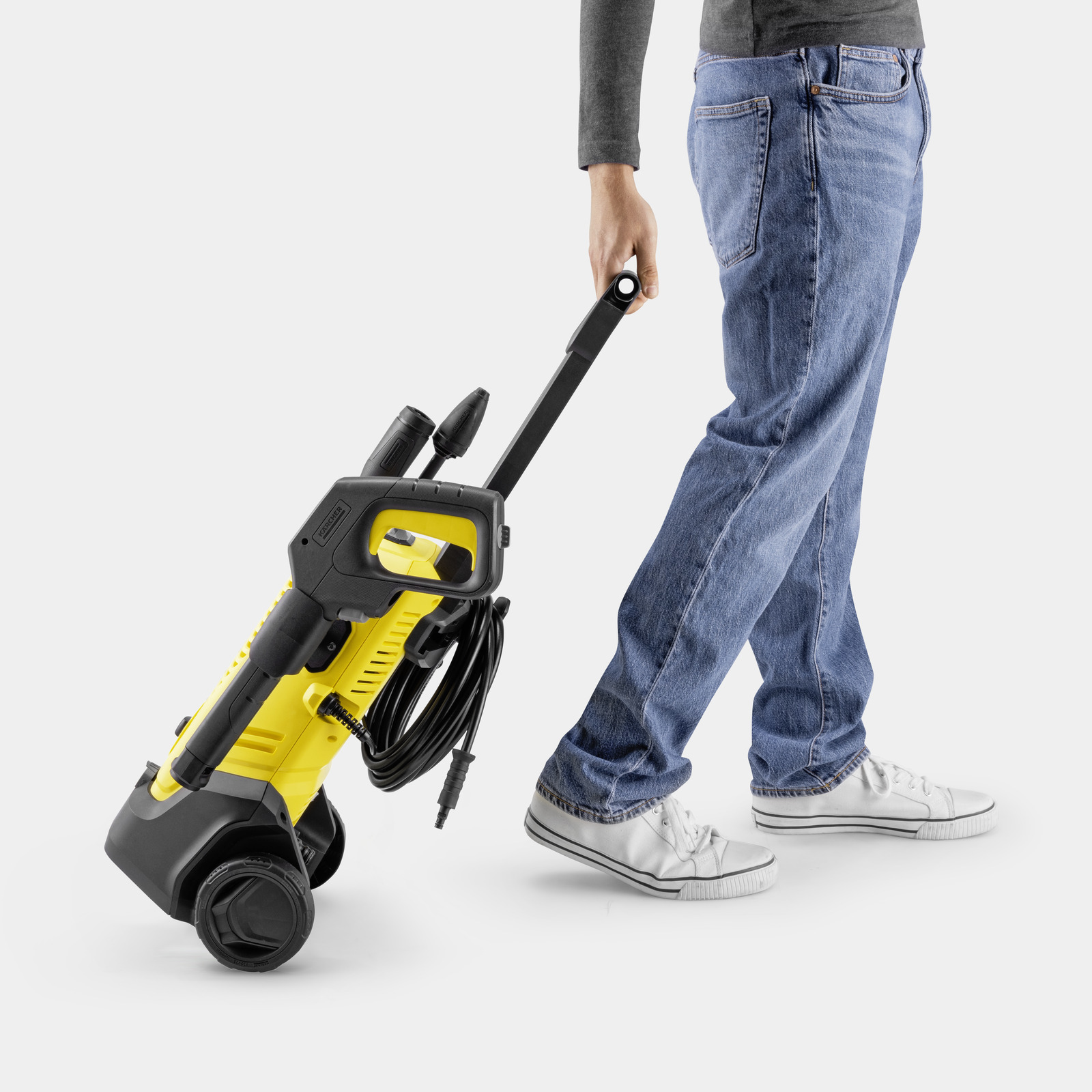 Eine Person in Jeans zieht einen gelb-schwarzen Hochdruckreiniger mit Rädern.