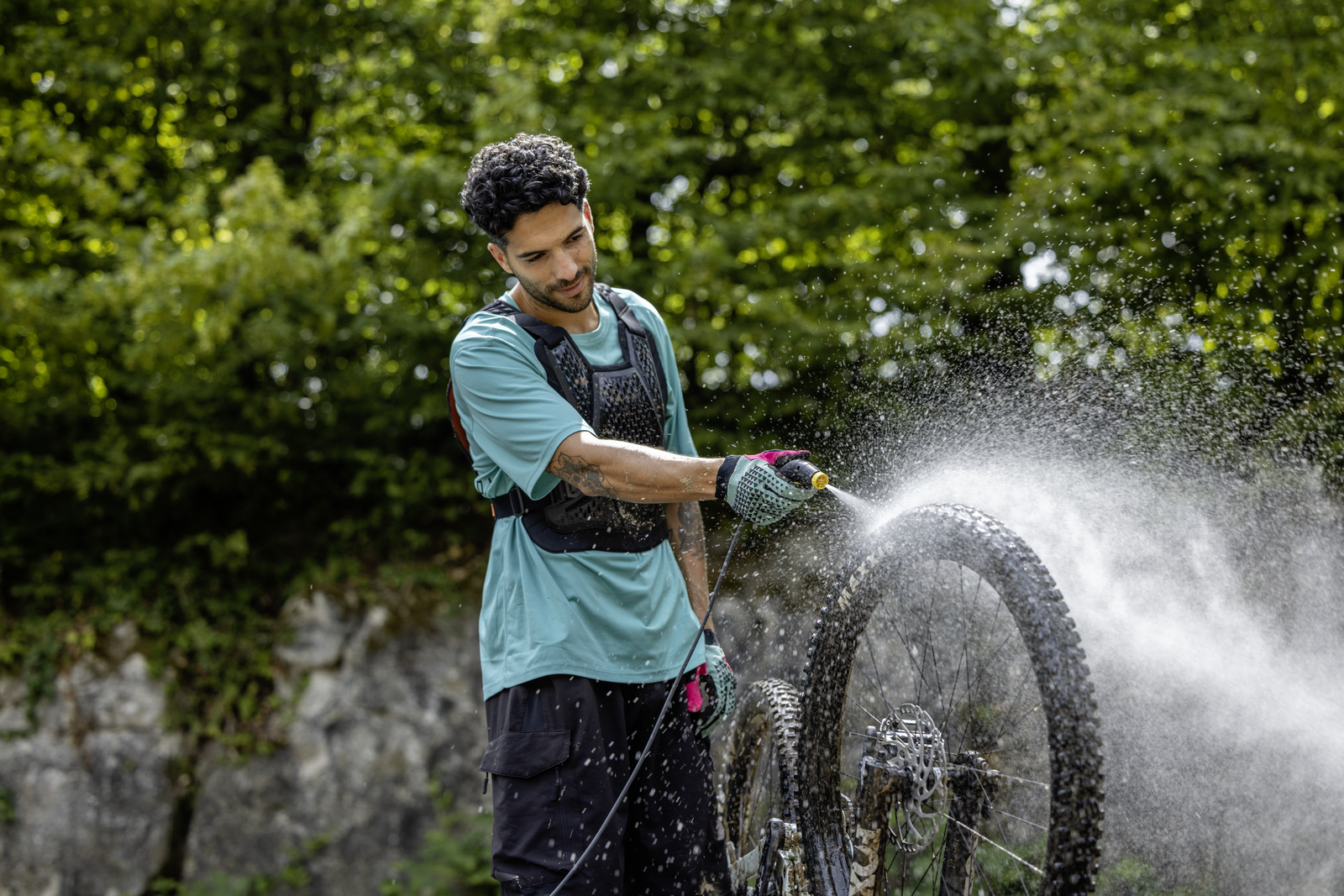 Un uomo con pettorina lava una ruota di mountain bike con un tubo.