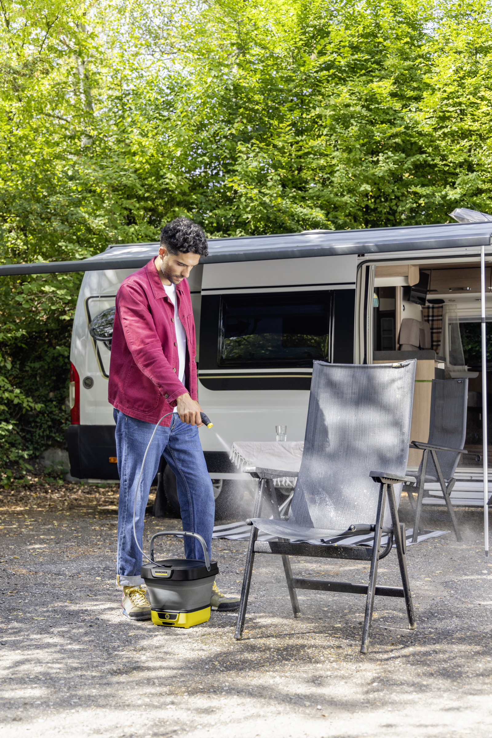 Uomo pulisce sedia da campeggio con idropulitrice vicino a camper.