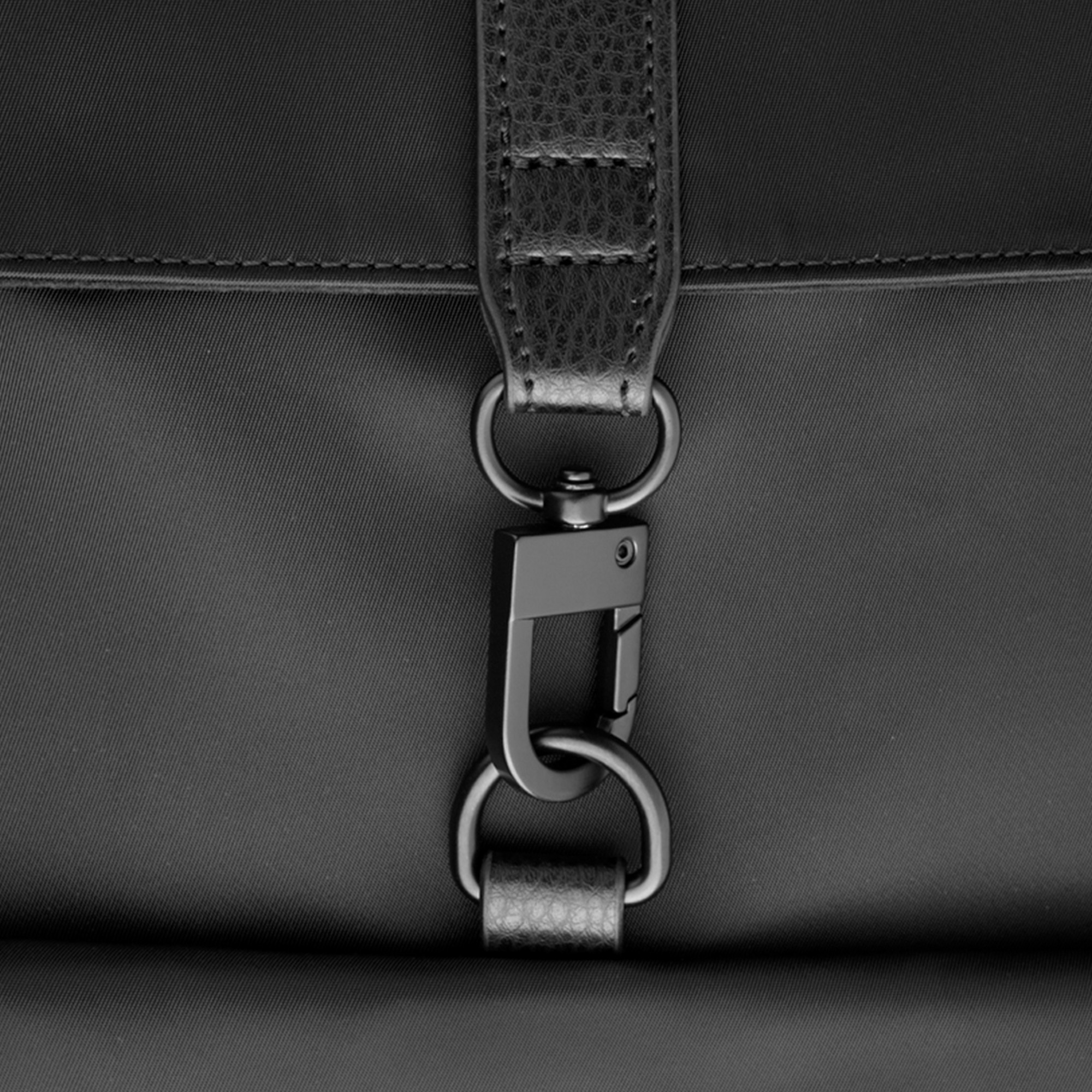 Moschettone in metallo nero con accenti in pelle su una borsa di tessuto.