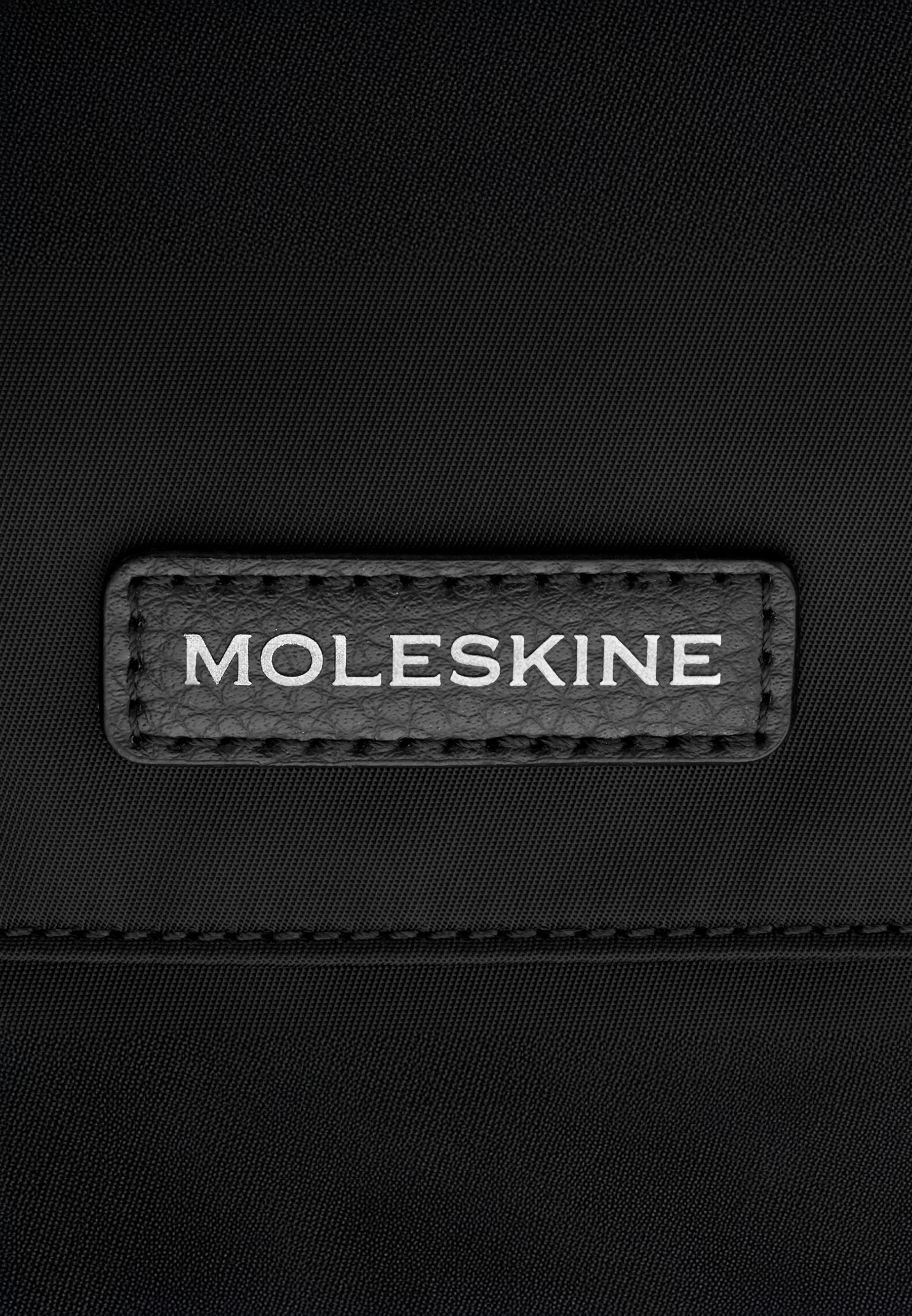 Etichetta in pelle nera con testo bianco 'MOLESKINE' su tessuto nero.