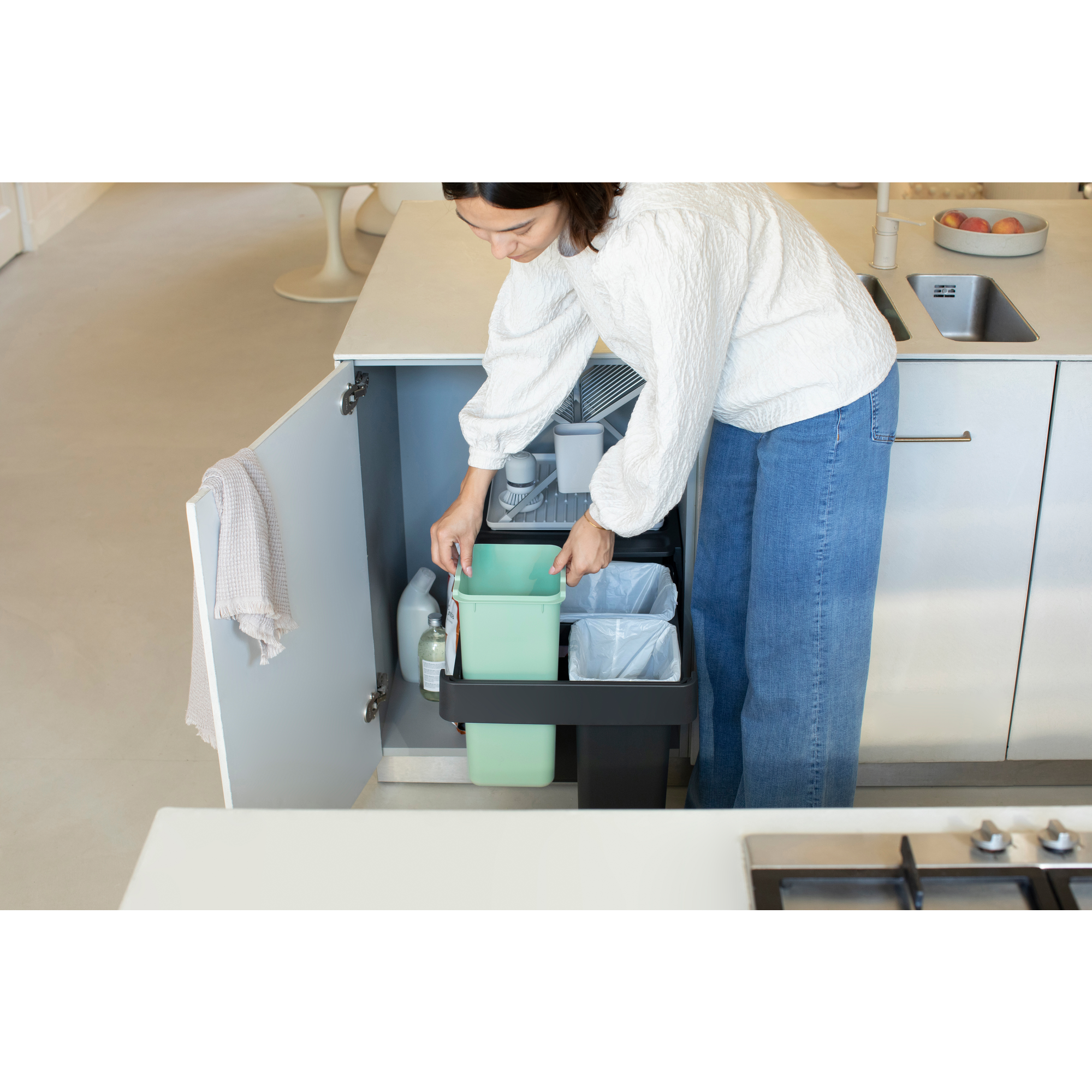 Une femme trie des déchets dans une poubelle intégrée dans une cuisine moderne.