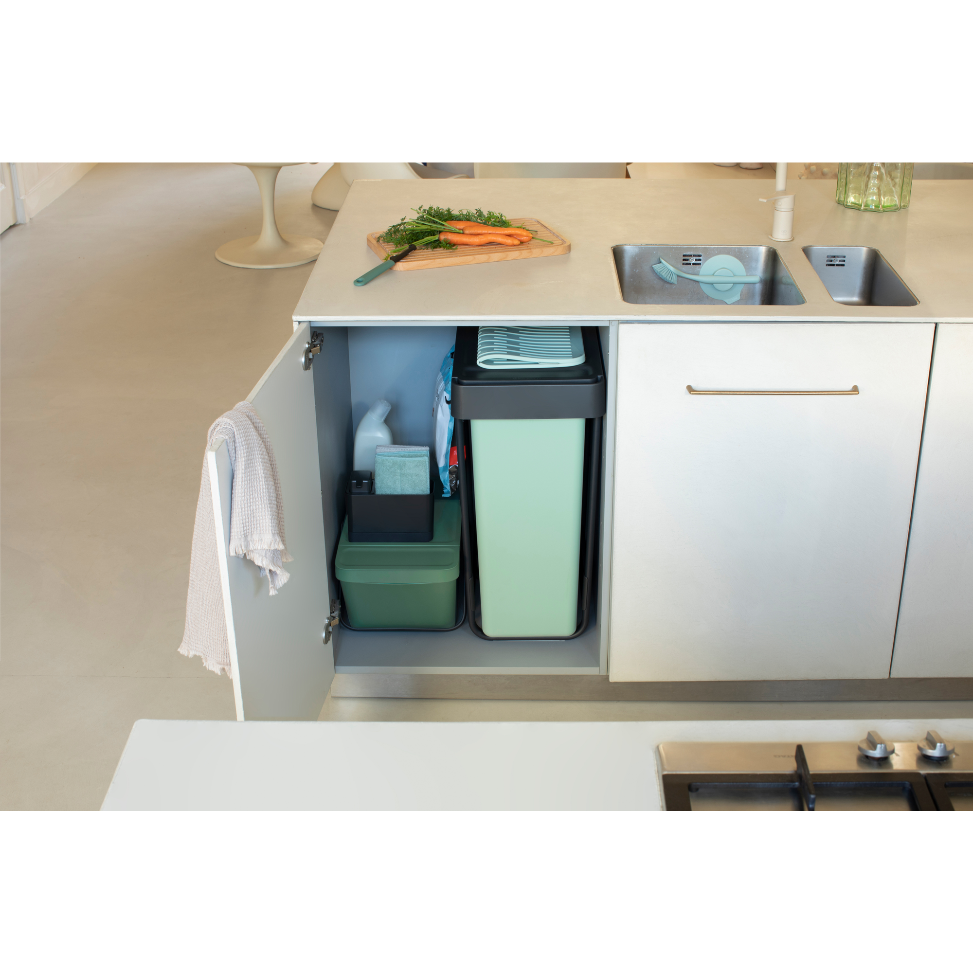 Placard de cuisine ouvert montrant poubelles, produits de nettoyage et carottes sur une planche.