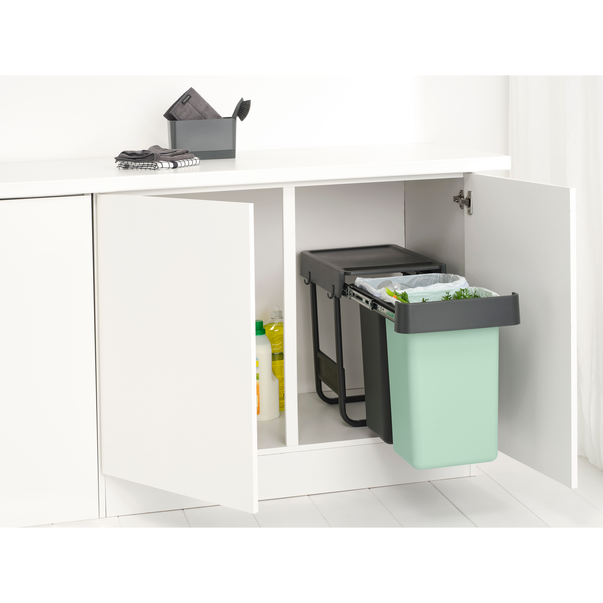 Two trash bins with lids and handles in a white storage unit. One is green.
