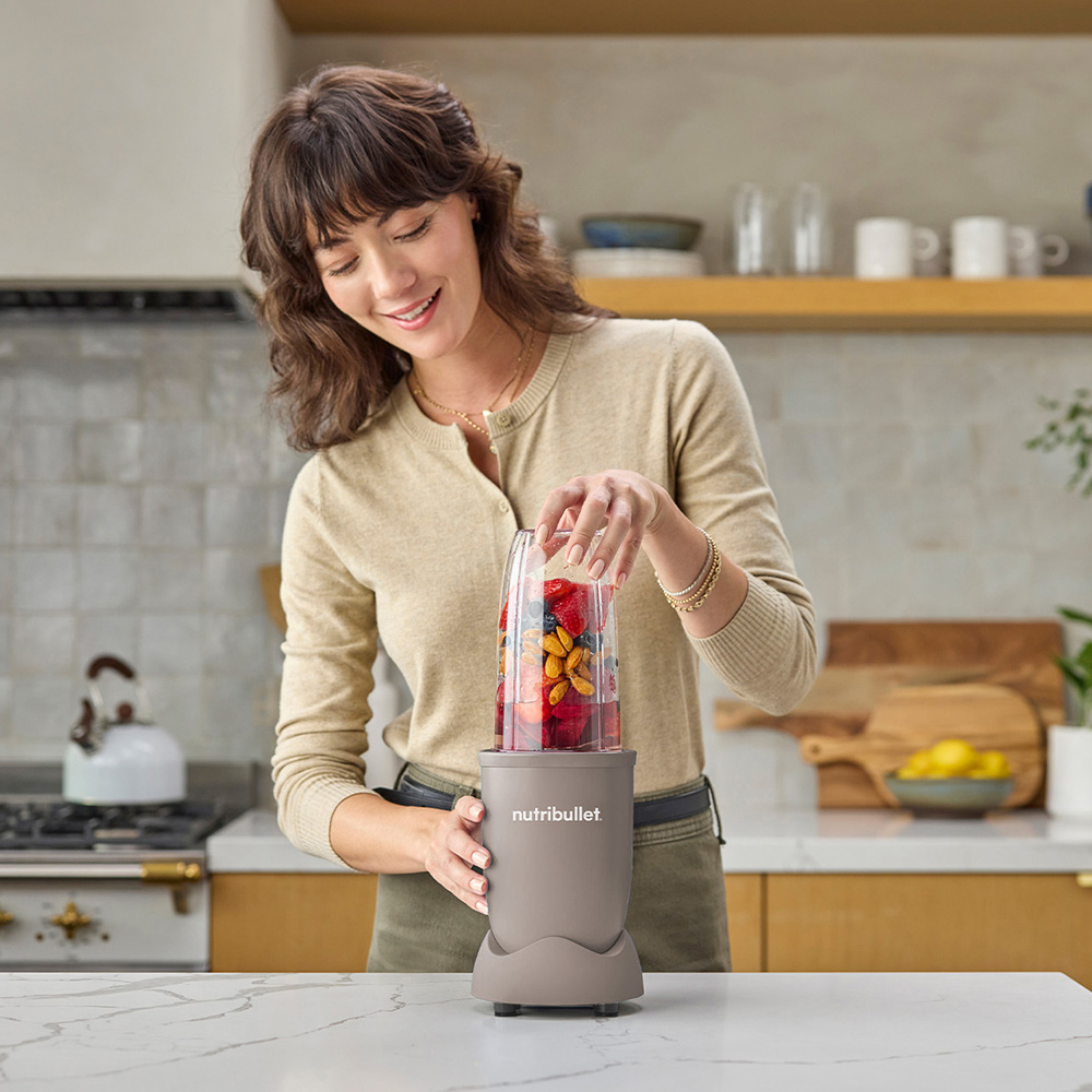 A woman prepares a fruit smoothie in a blender in a kitchen.