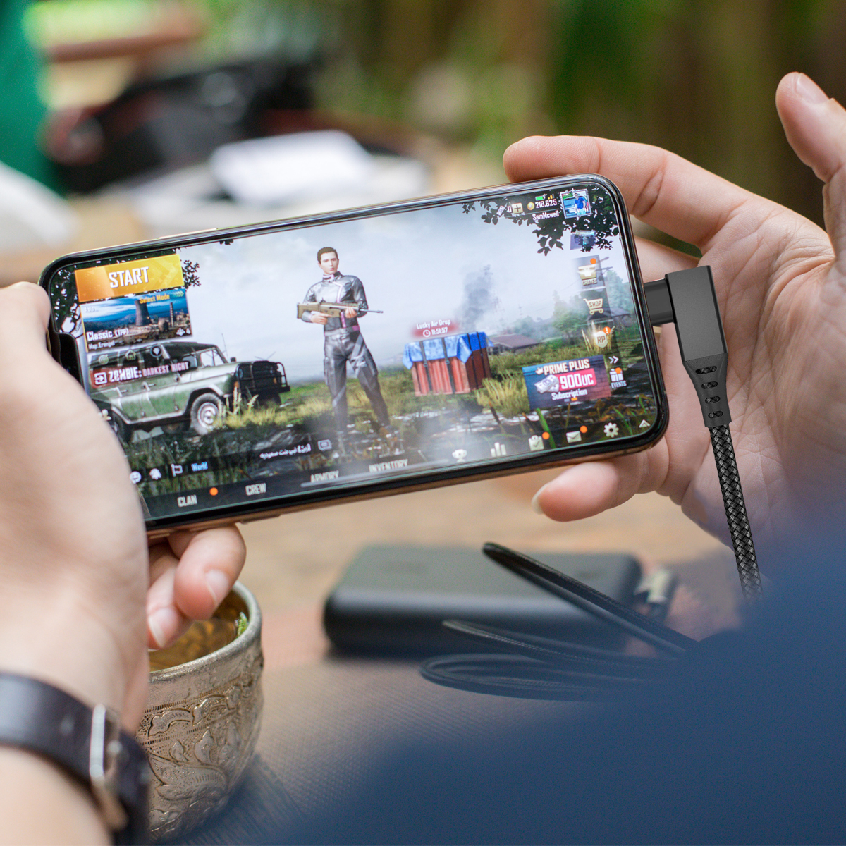 Mani tengono un telefono che mostra un menu di gioco, con un cavo di ricarica collegato.
