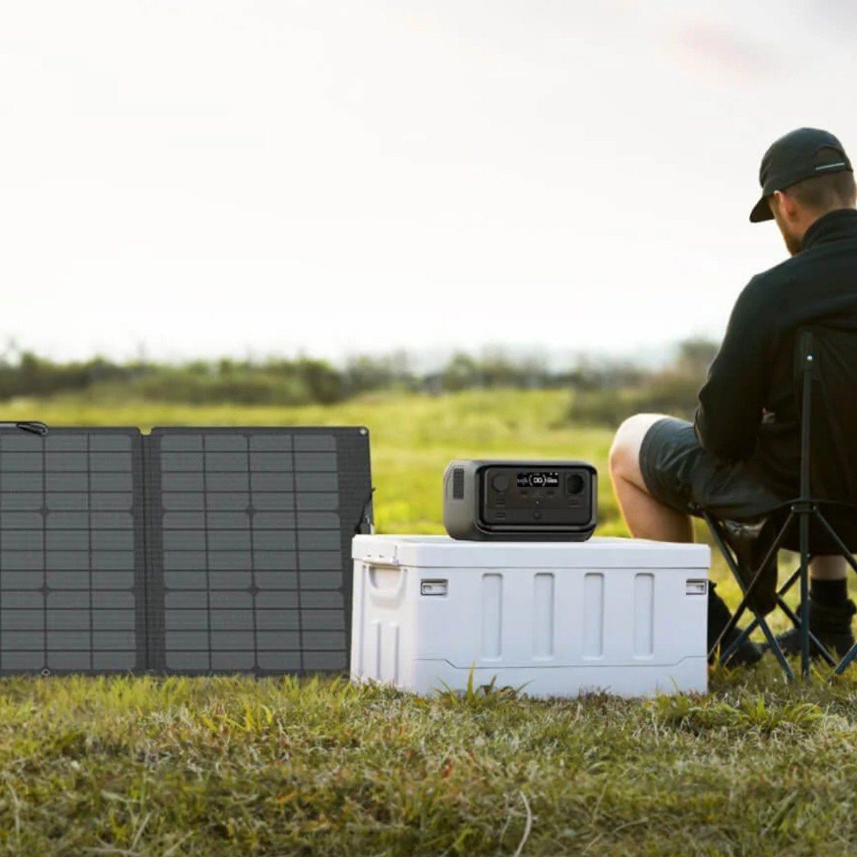 Un uomo seduto all'aperto vicino a un pannello solare pieghevole, una scatola portaoggetti bianca e una centrale elettrica portatile.