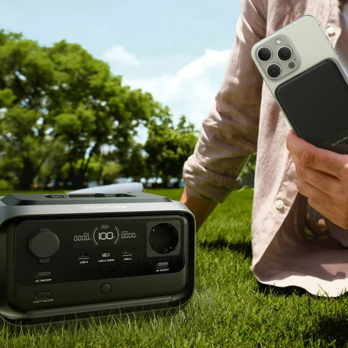 Una centrale elettrica portatile e uno smartphone sull'erba, alberi sullo sfondo.