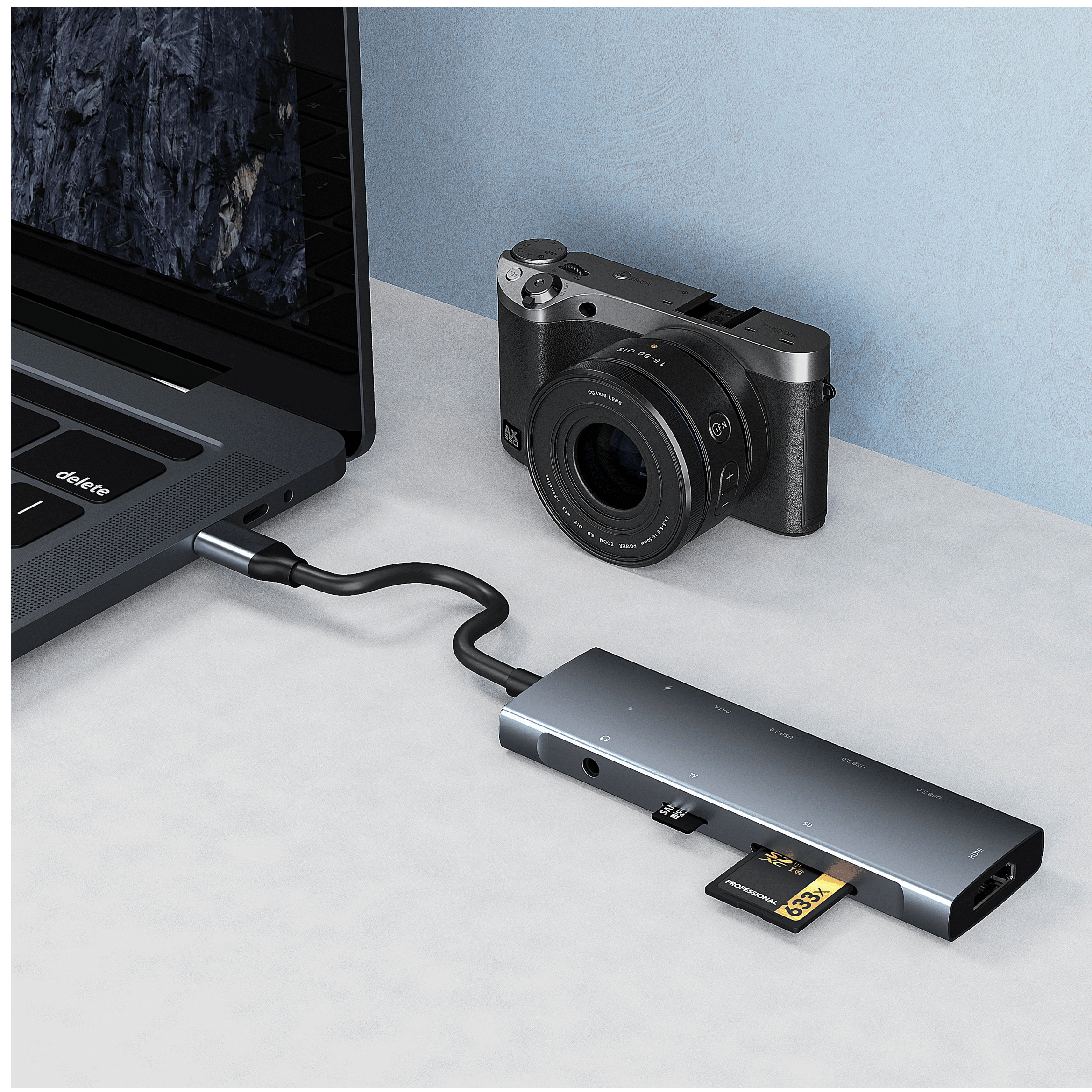 Een laptop, camera en USB-hub met SD- en HDMI-poorten op een bureau.