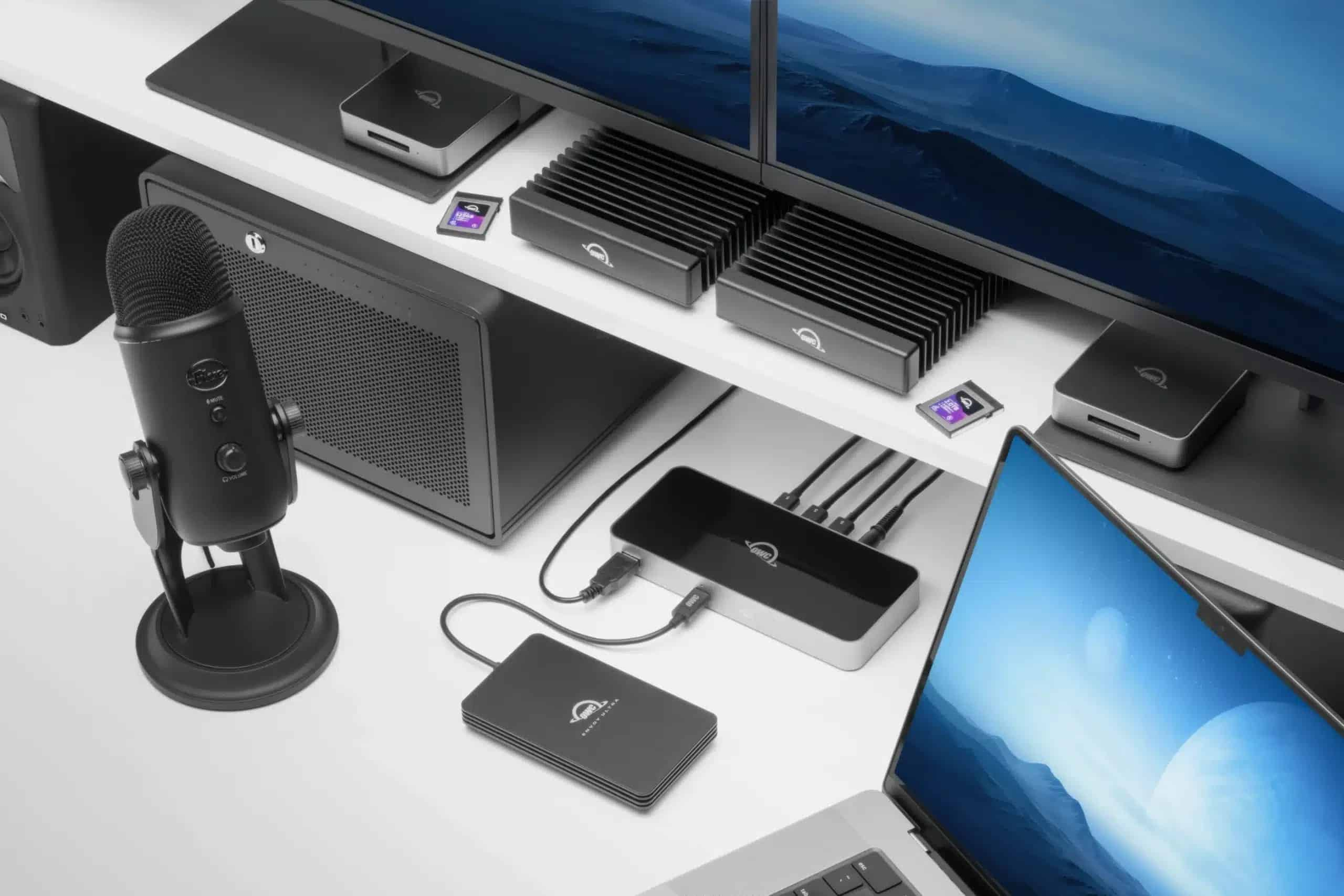 Zwarte microfoon, externe schijven, hub en laptop op een wit bureau.