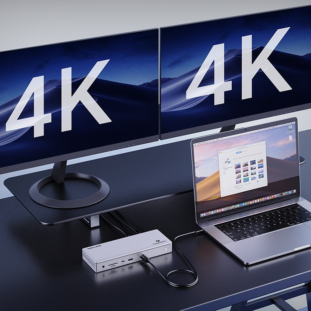 Twee monitoren met "4K" flankeren een laptop en dockingstation op een bureau.