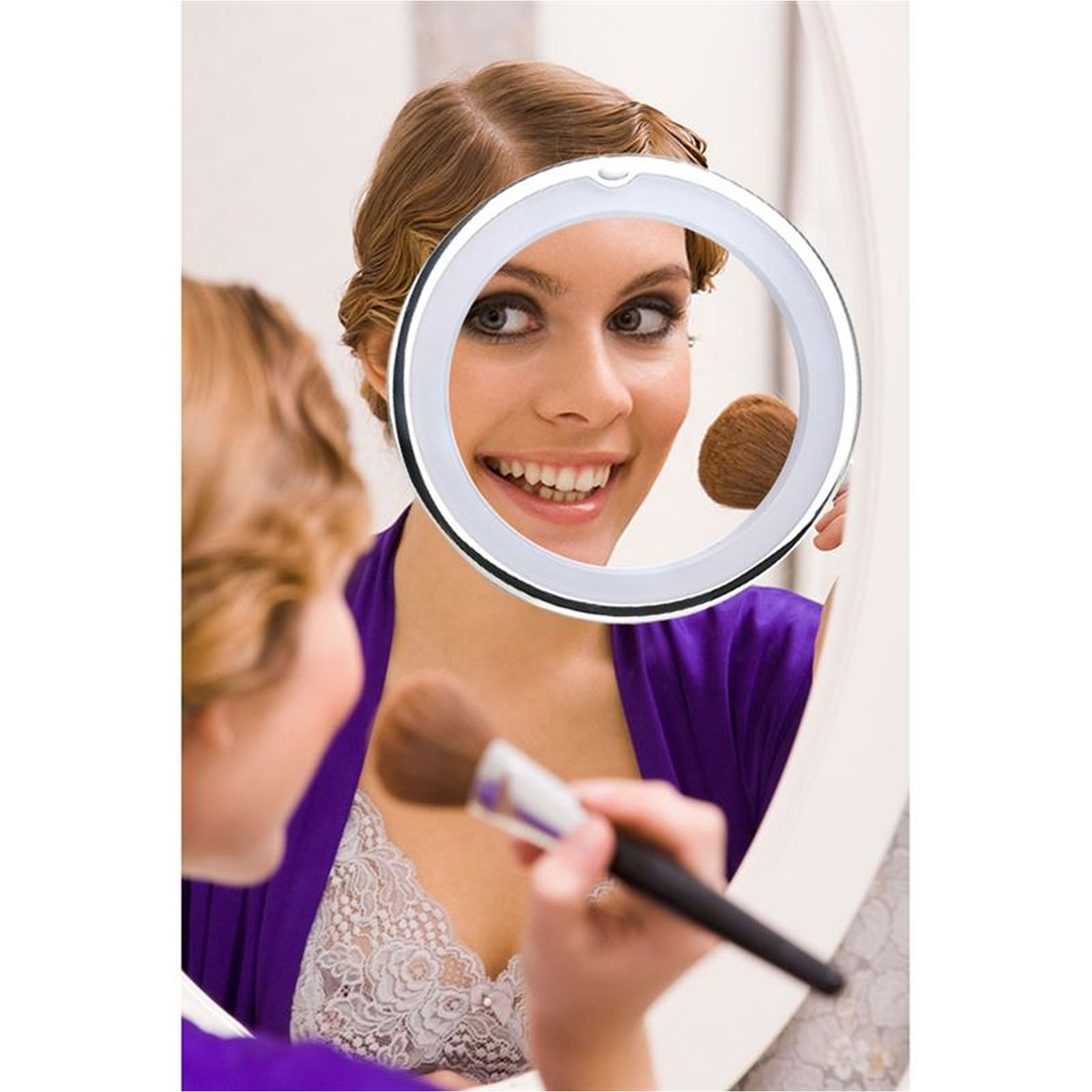 Una donna si trucca con un pennello davanti a uno specchio illuminato.