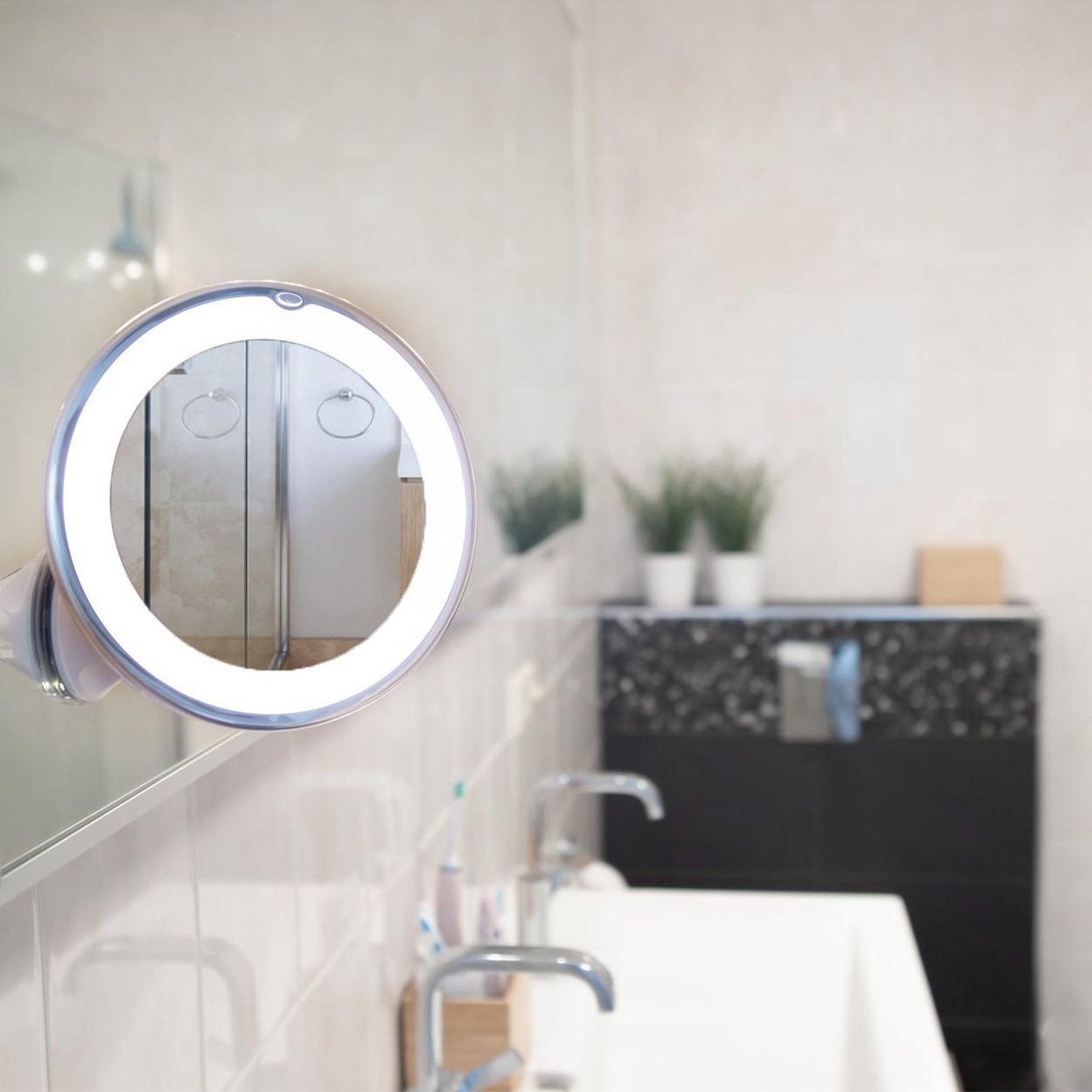 Specchio per il trucco illuminato sopra un lavandino, con piante sullo sfondo.