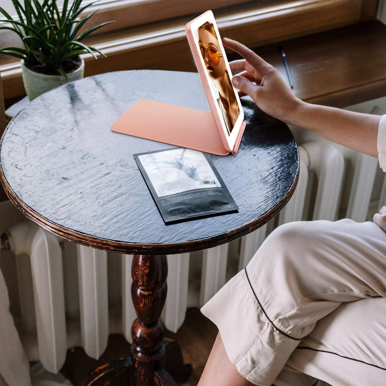 Una donna tiene un telefono specchio per il trucco illuminato con un viso sullo schermo.