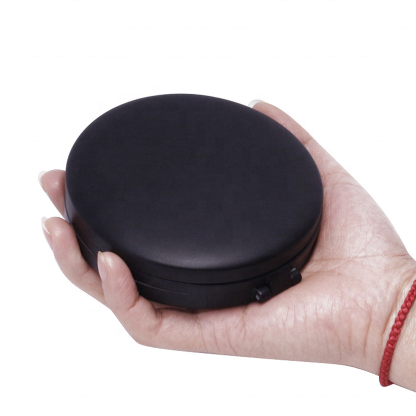 Una mano tiene un dispositivo elettronico nero, rotondo e chiuso con un braccialetto intrecciato rosso.