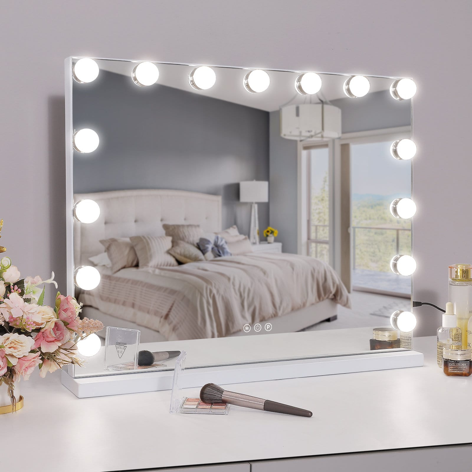 Specchio Hollywood con luci su un tavolino da trucco davanti a un letto.