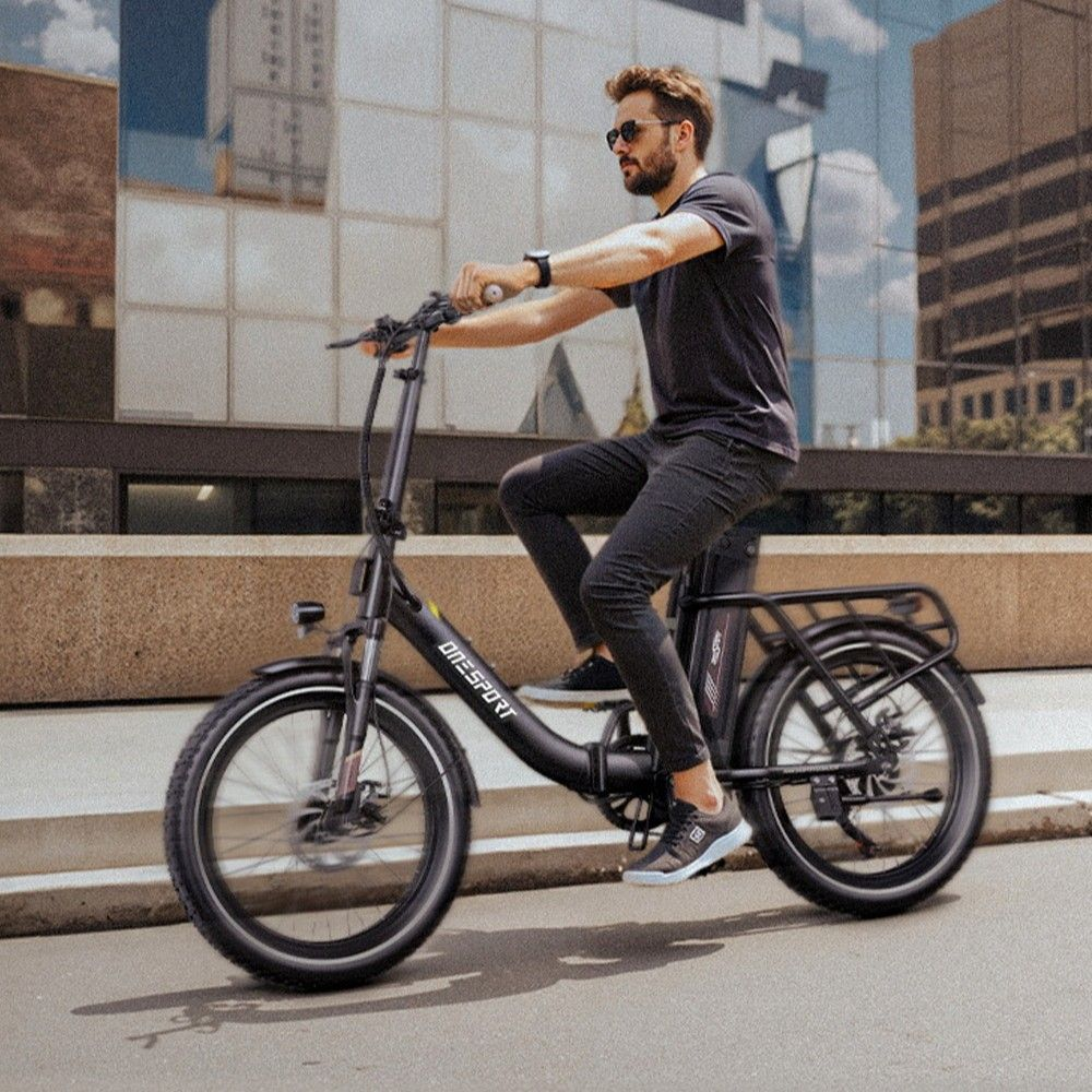 Hombre con gafas de sol monta una e-bike negra en calle de ciudad con edificios modernos.