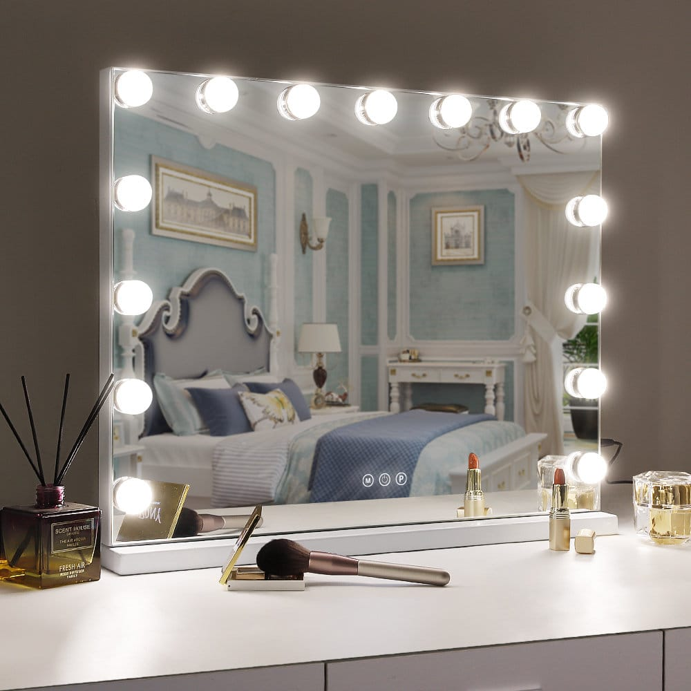 Uno specchio per il trucco illuminato riflette una camera da letto. Pennelli e rossetti sul mobile.