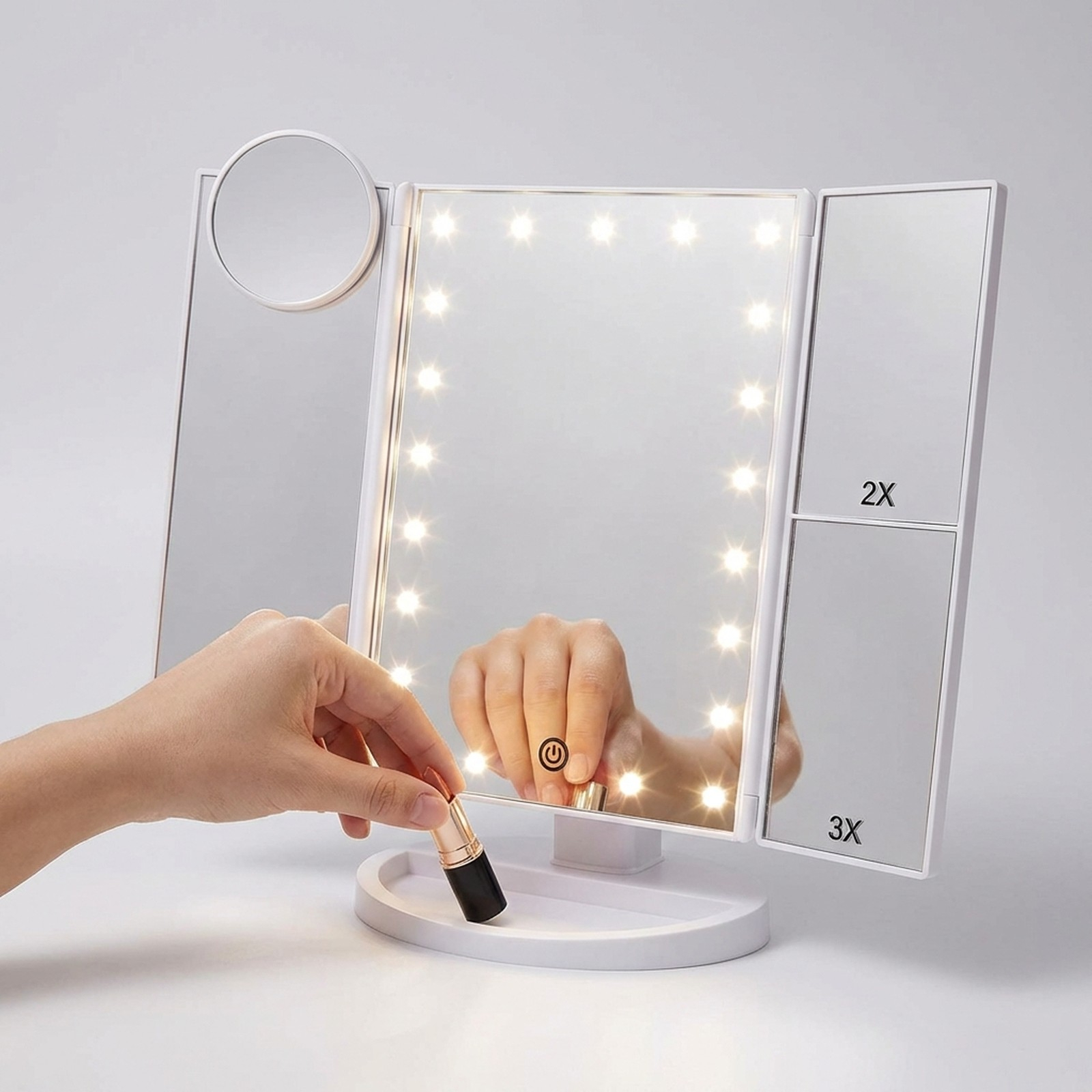Una mano tiene un rossetto vicino a uno specchio per il trucco illuminato a tre pannelli.