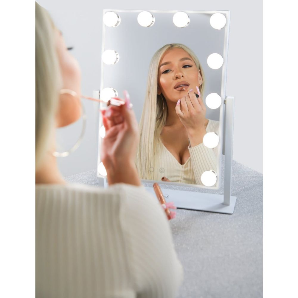 Una donna bionda si applica il rossetto davanti a uno specchio illuminato.