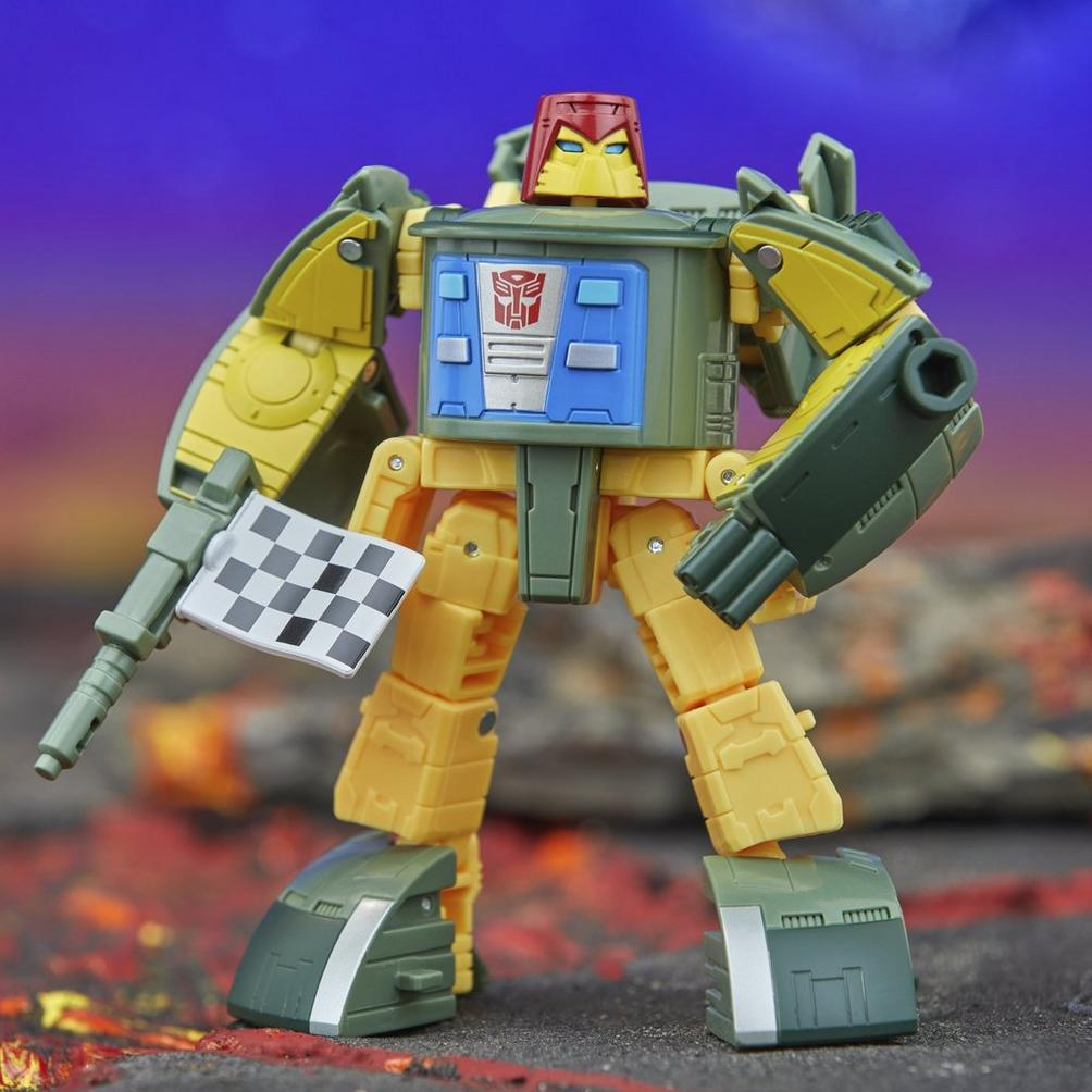 Żółty i zielony robot Transformer z czerwonym hełmem trzyma czarno-białą flagę w szachownicę.
