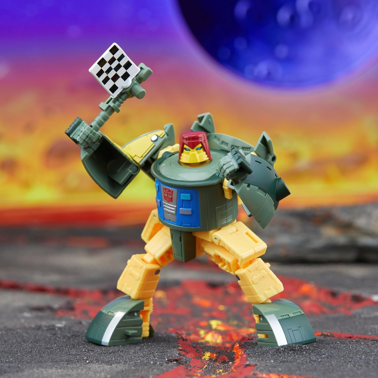 Zielony robot z żółtymi nogami trzyma zabawkowaty młotek z flagą wyścigową w kratkę.