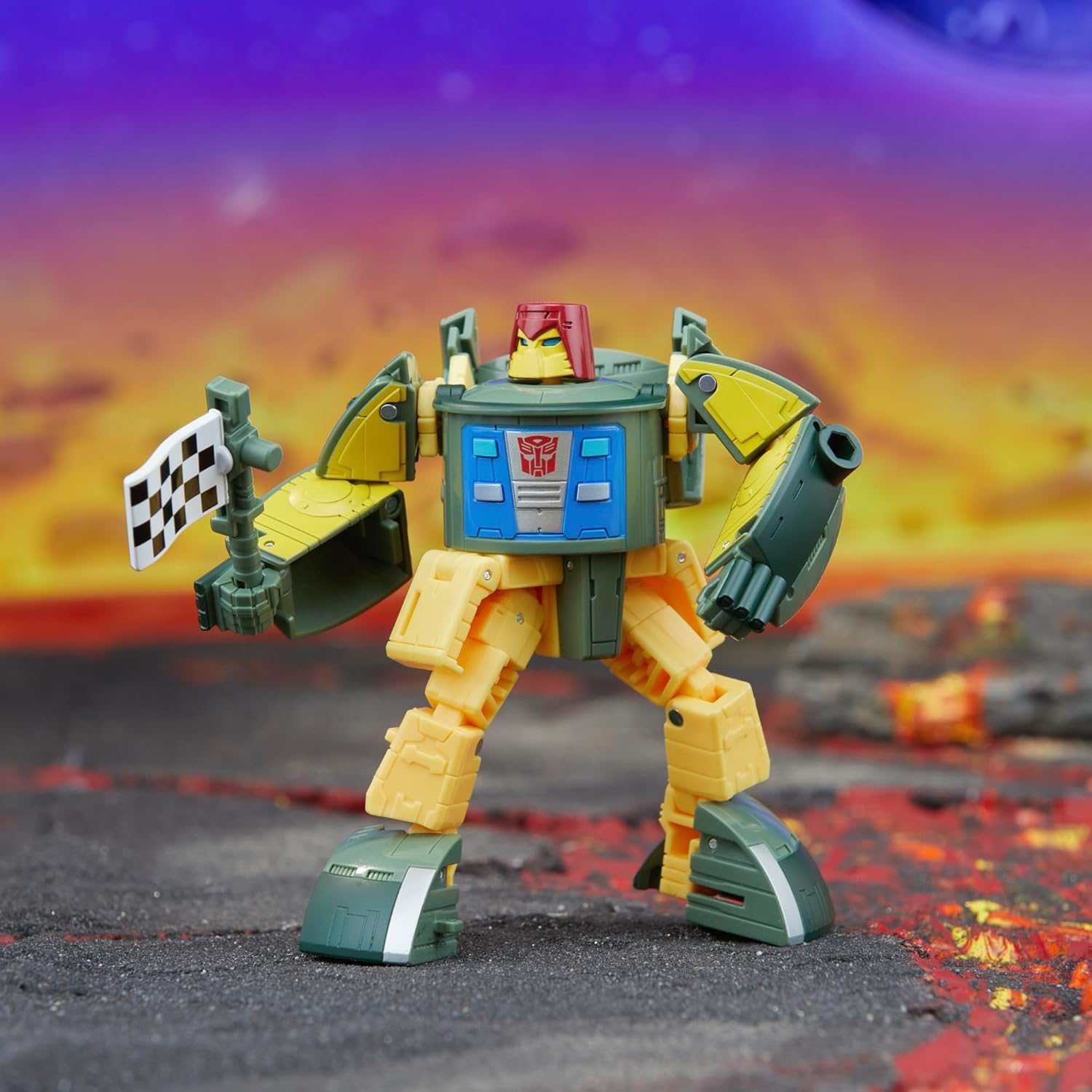 Żółto-zielona figurka robota z szachownicą flagą, na tle ognistego tła.