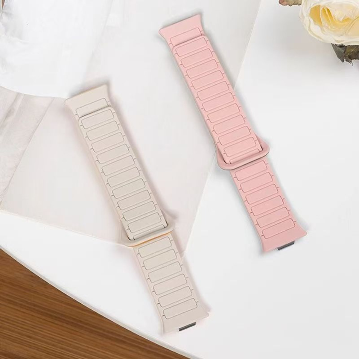 Zwei magnetische Armbänder, eines hellbeige, eines rosa, auf weißem Hintergrund.