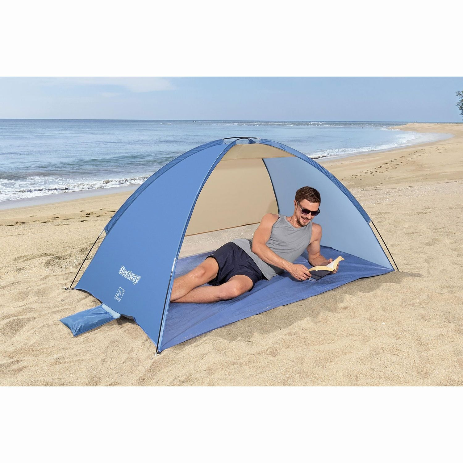 Man leest in een blauwe strandtent op een zandstrand met de oceaan op de achtergrond.