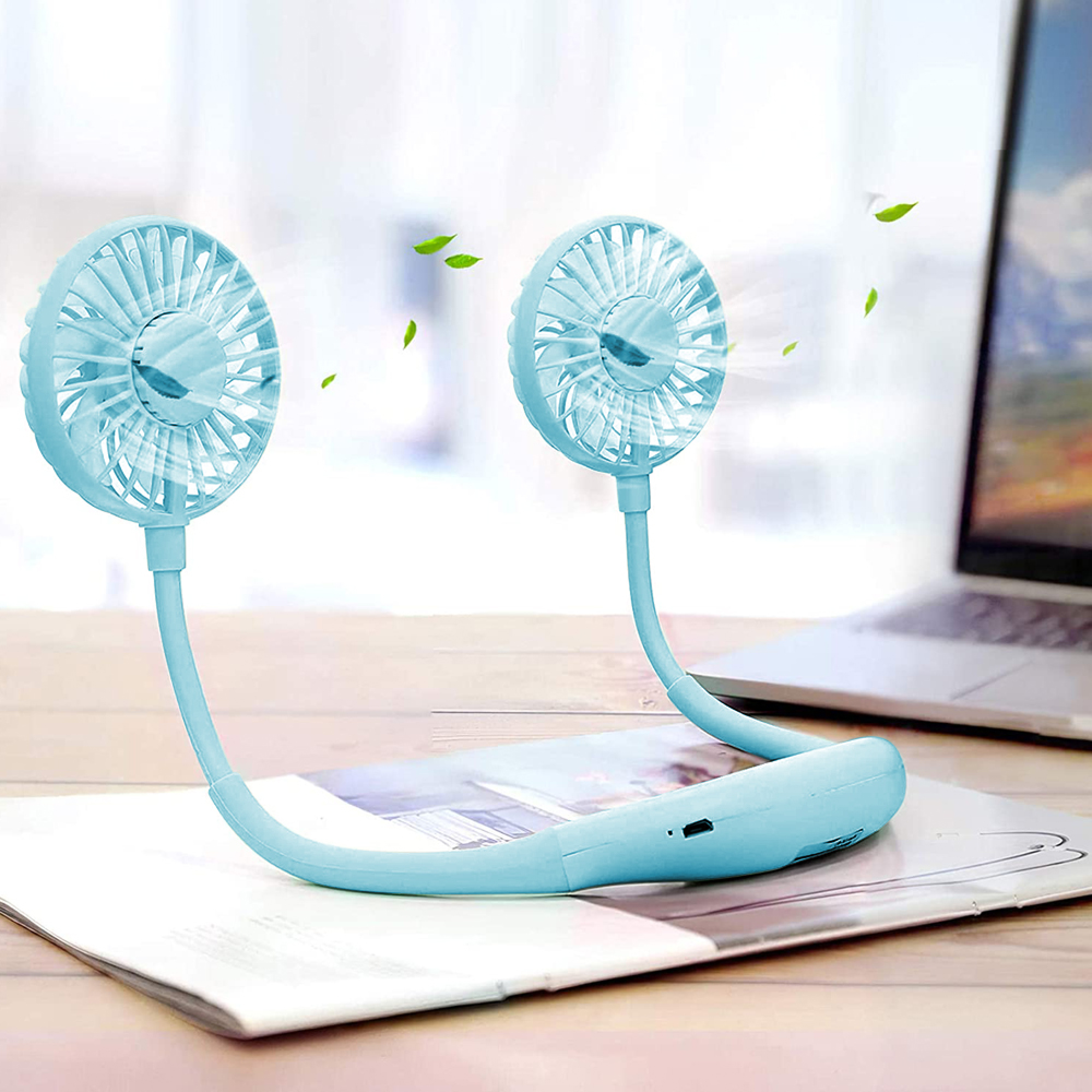 Ein hellblauer Nackenventilator liegt auf einem Magazin neben einem Laptop.