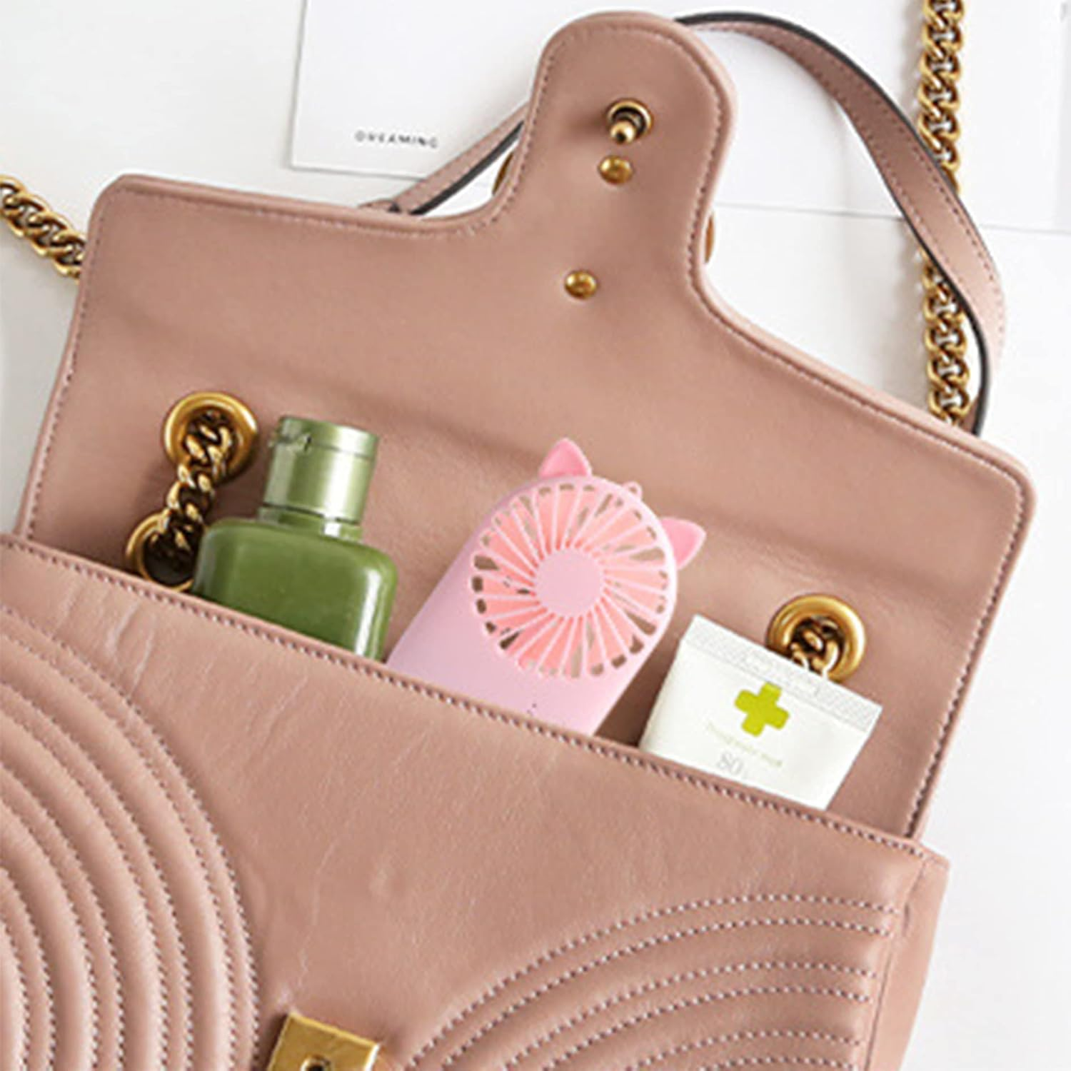 Eine rosafarbene Tasche mit einem kleinen Ventilator, einer grünen Flasche und einer Tube.