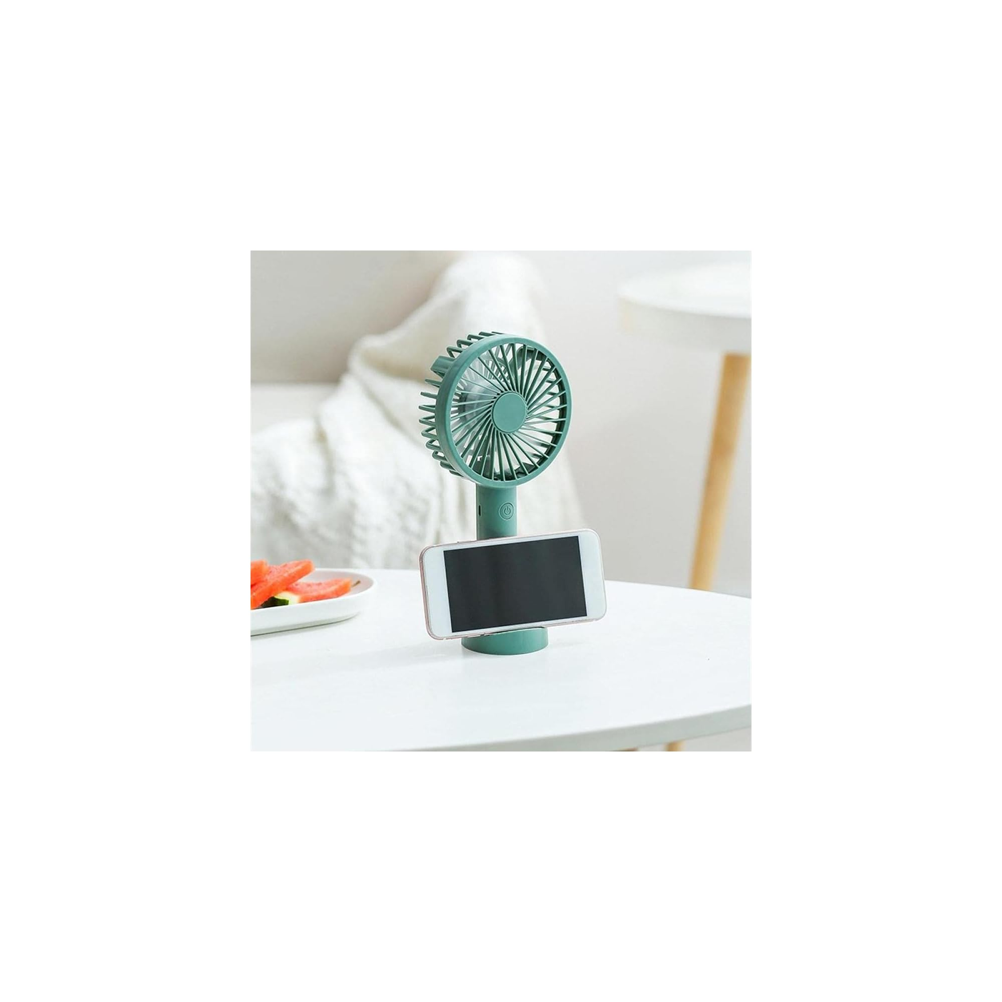 Ein grüner Mini-Ventilator steht auf einem weißen Tisch hinter einem Smartphone.