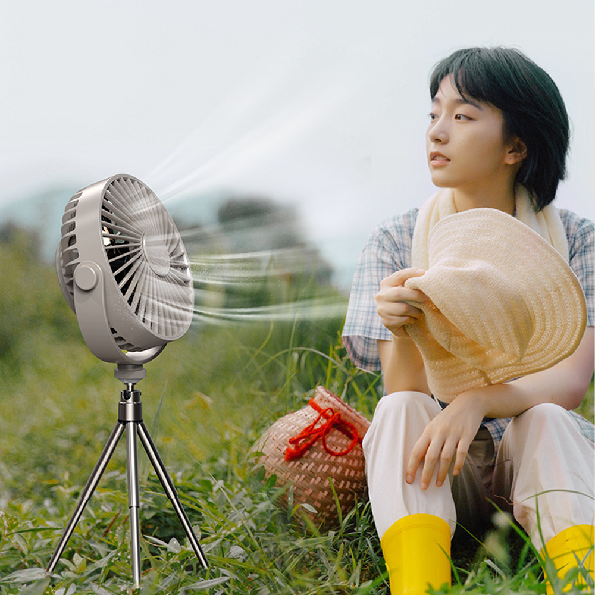 Ein tragbarer Ventilator kühlt eine Person im Freien auf einer Wiese.
