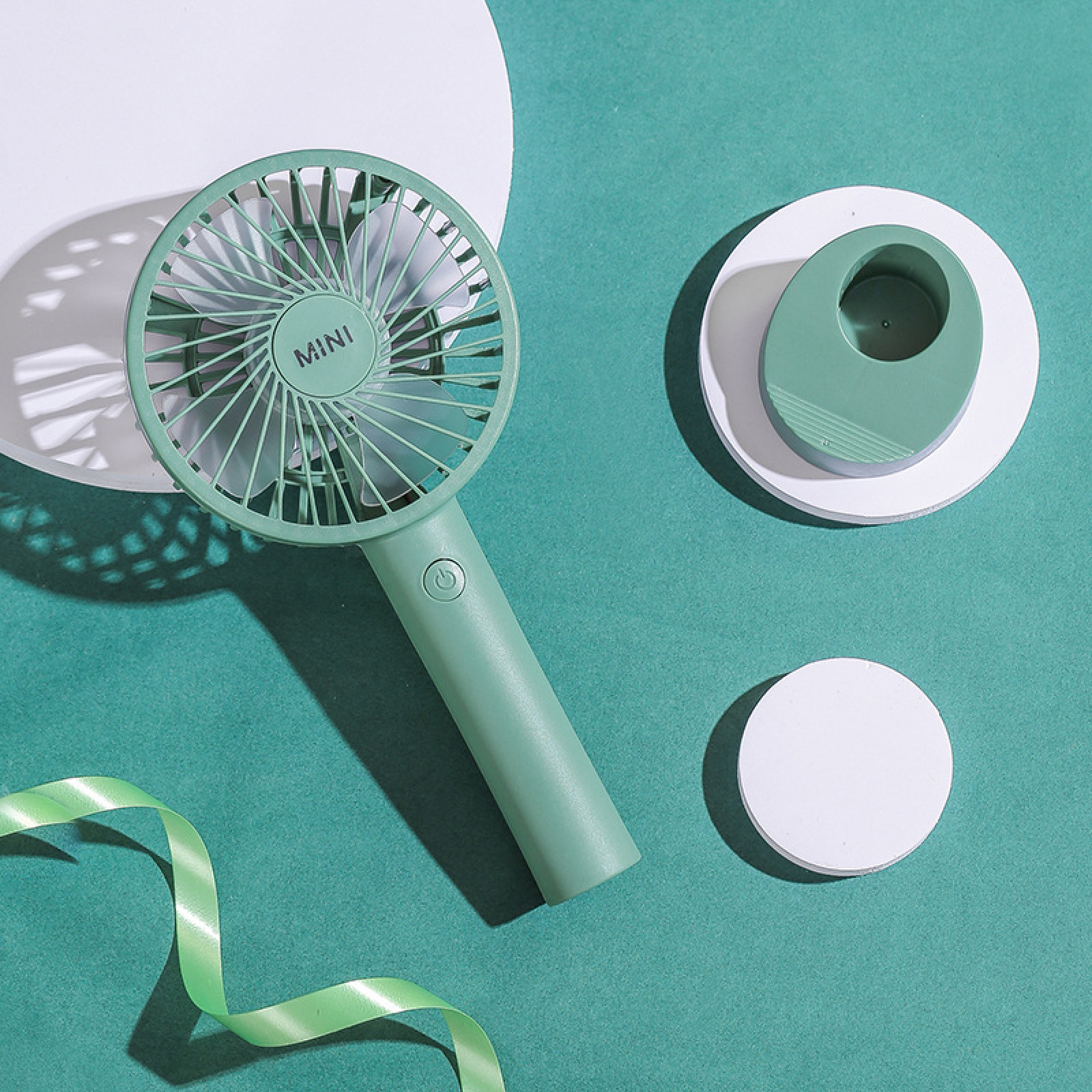 Ein kleiner grüner Ventilator liegt auf einem türkisfarbenen Hintergrund mit weißen Kreisen.