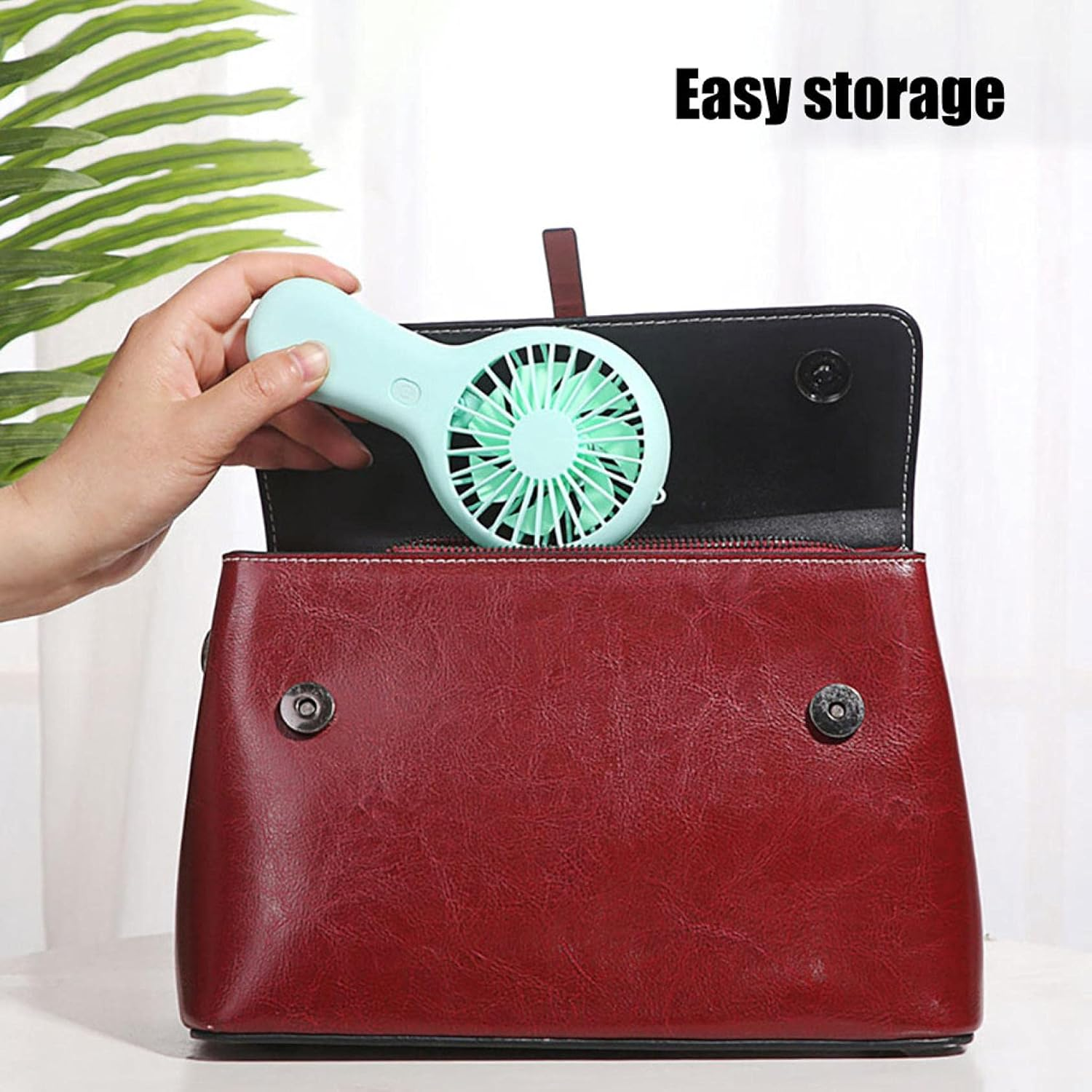 Eine Hand legt einen mintgrünen Mini-Ventilator in eine rote Tasche.