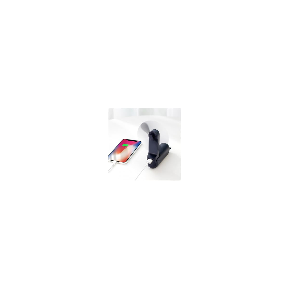 Ein schwarzer USB-Ventilator lädt ein Smartphone auf, das auf einer weißen Oberfläche liegt.